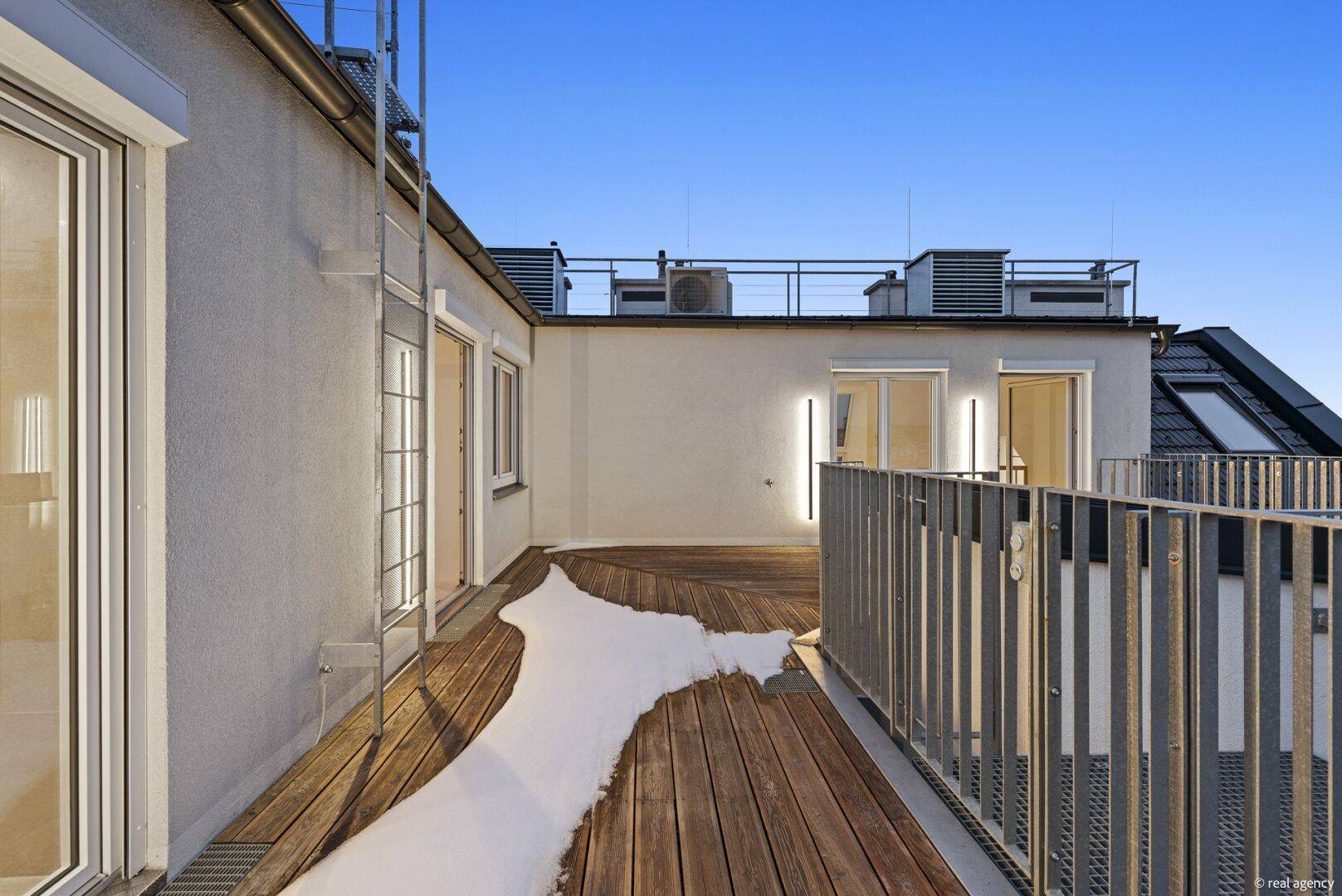 Dachterrasse bei Dämmerung mit Holzboden, Metallgeländer und Blick auf die Stadt.