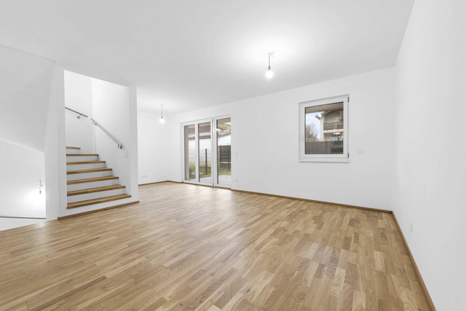 Geräumiges, leeres Wohnzimmer mit Holzboden und Zugang zur Terrasse.