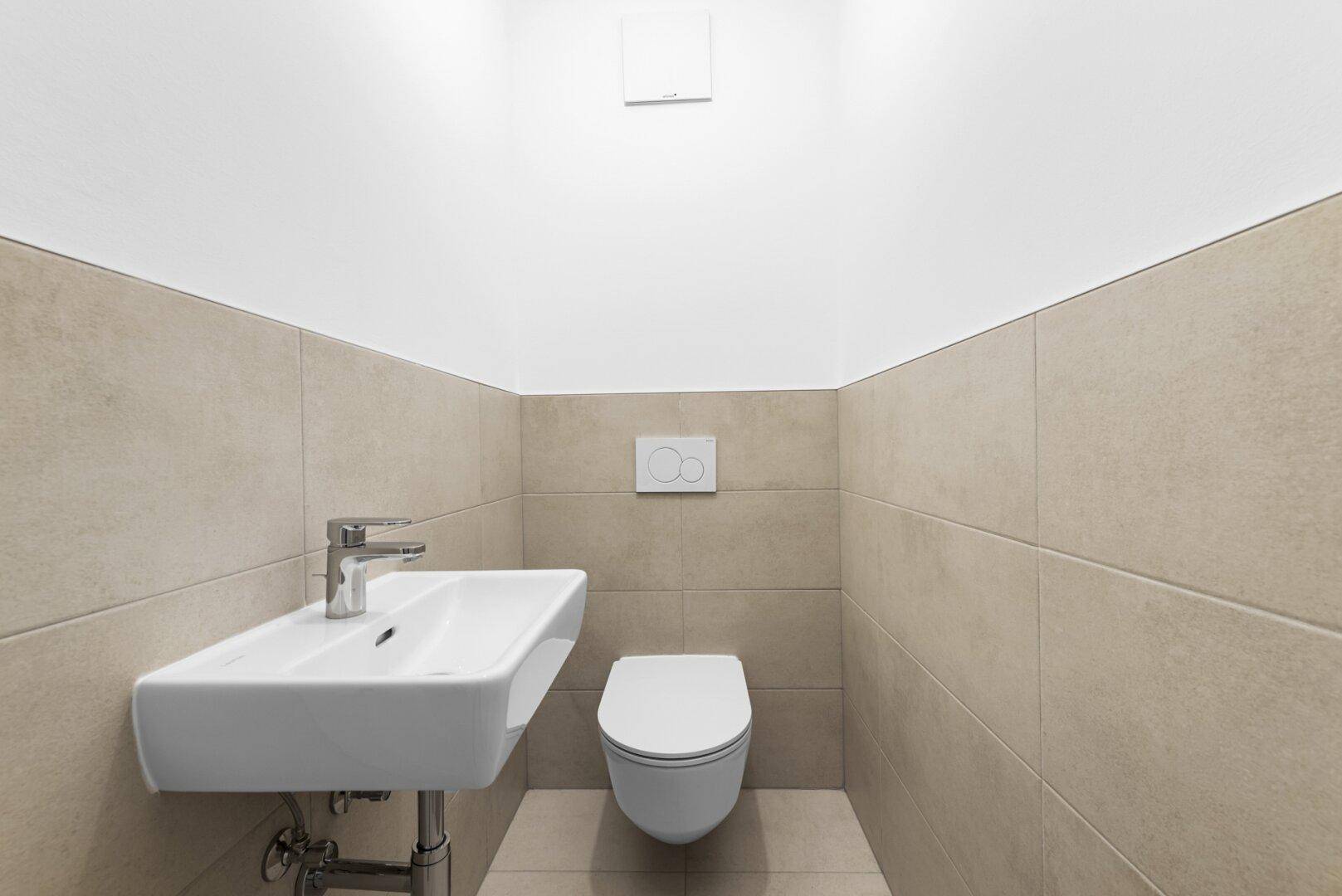 Modernes Gäste-WC mit beigefarbenen Fliesen, wandhängendem WC und kleinem Waschbecken.