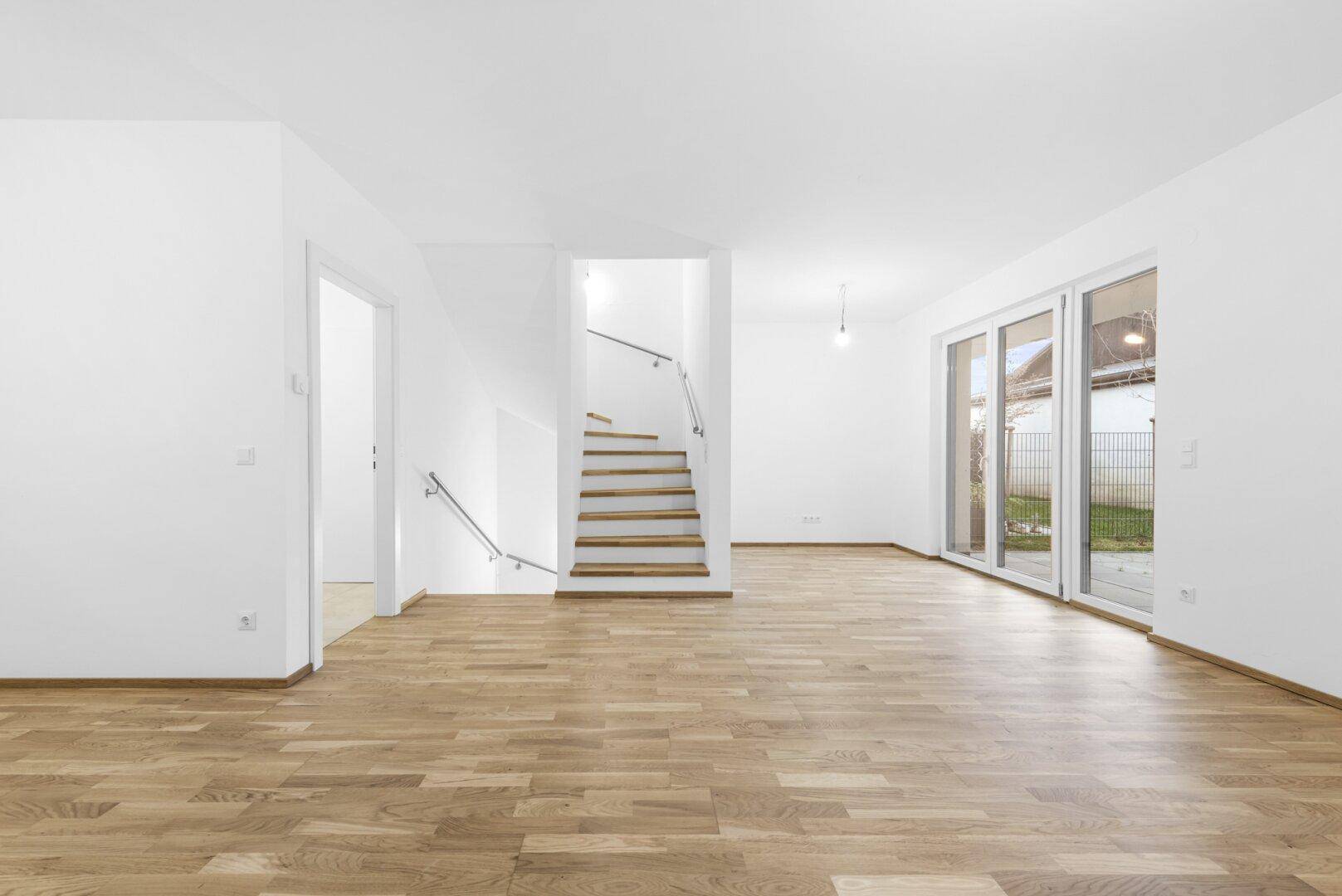 Großzügiger Wohnbereich mit Holzboden, Treppe und breiter Terrassentür.