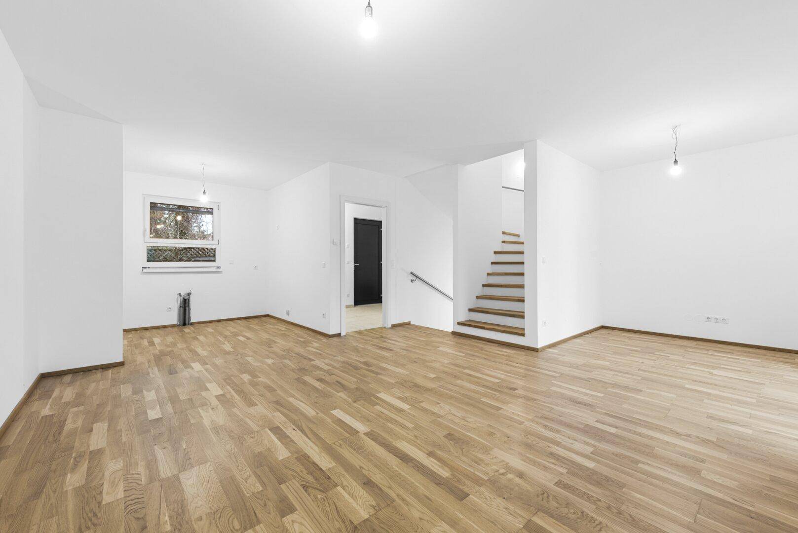 Heller Wohnbereich mit Holzboden, Treppe und Fenster mit Blick ins Grüne.