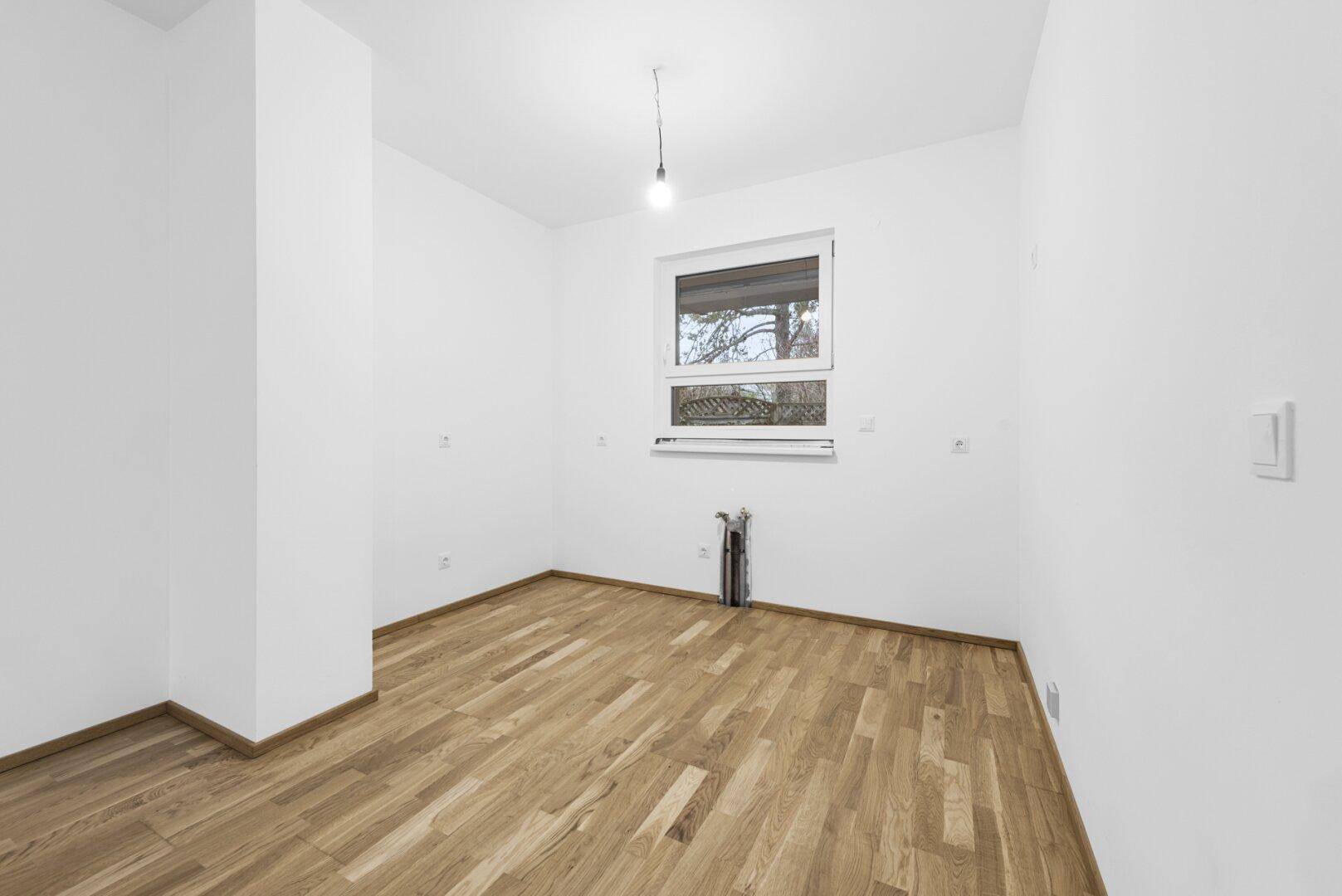 Leerer Raum mit Holzboden und Fenster, ideal als Schlaf- oder Arbeitszimmer.