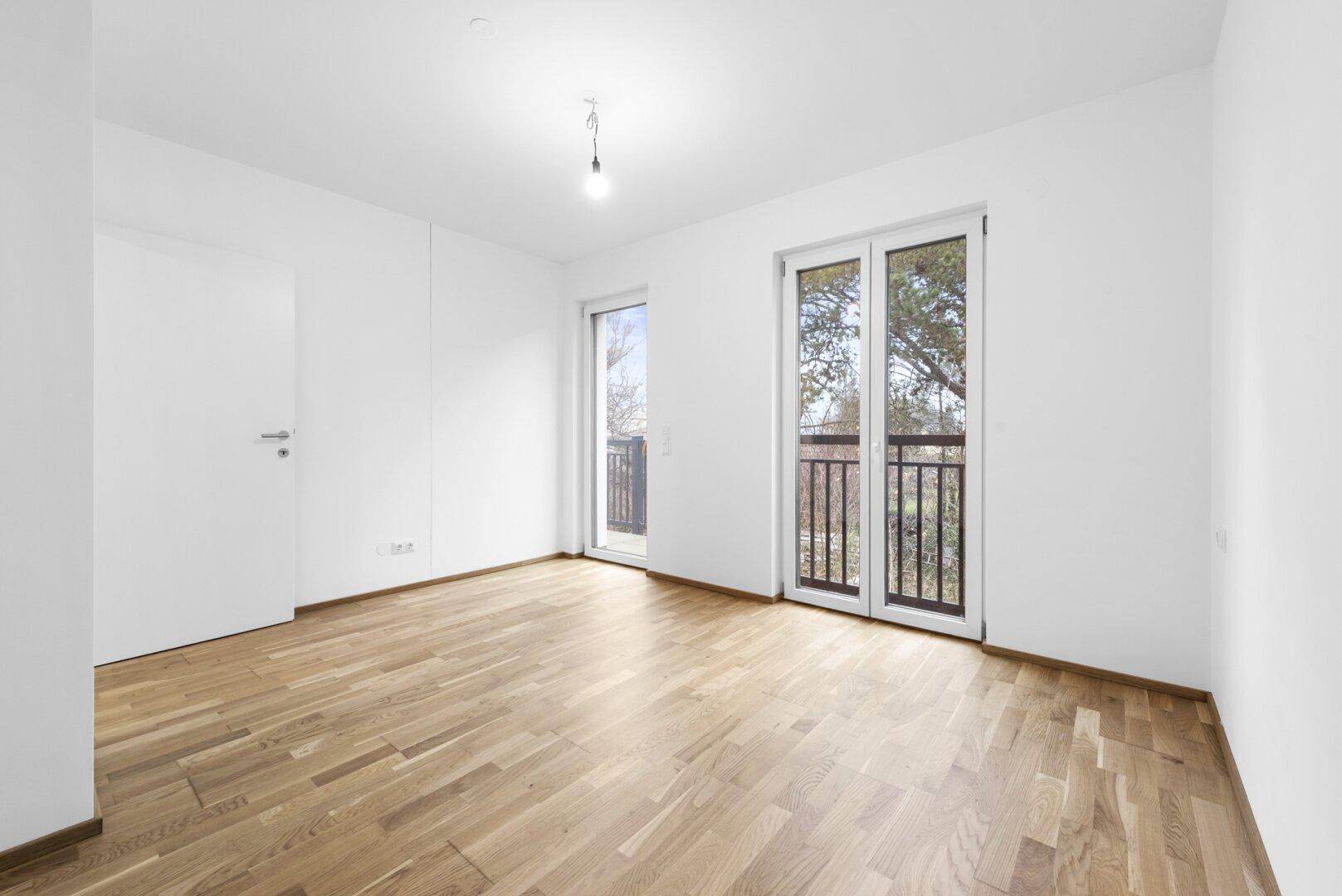 Helles Schlafzimmer mit Holzboden und Zugang zu einem französischen Balkon.