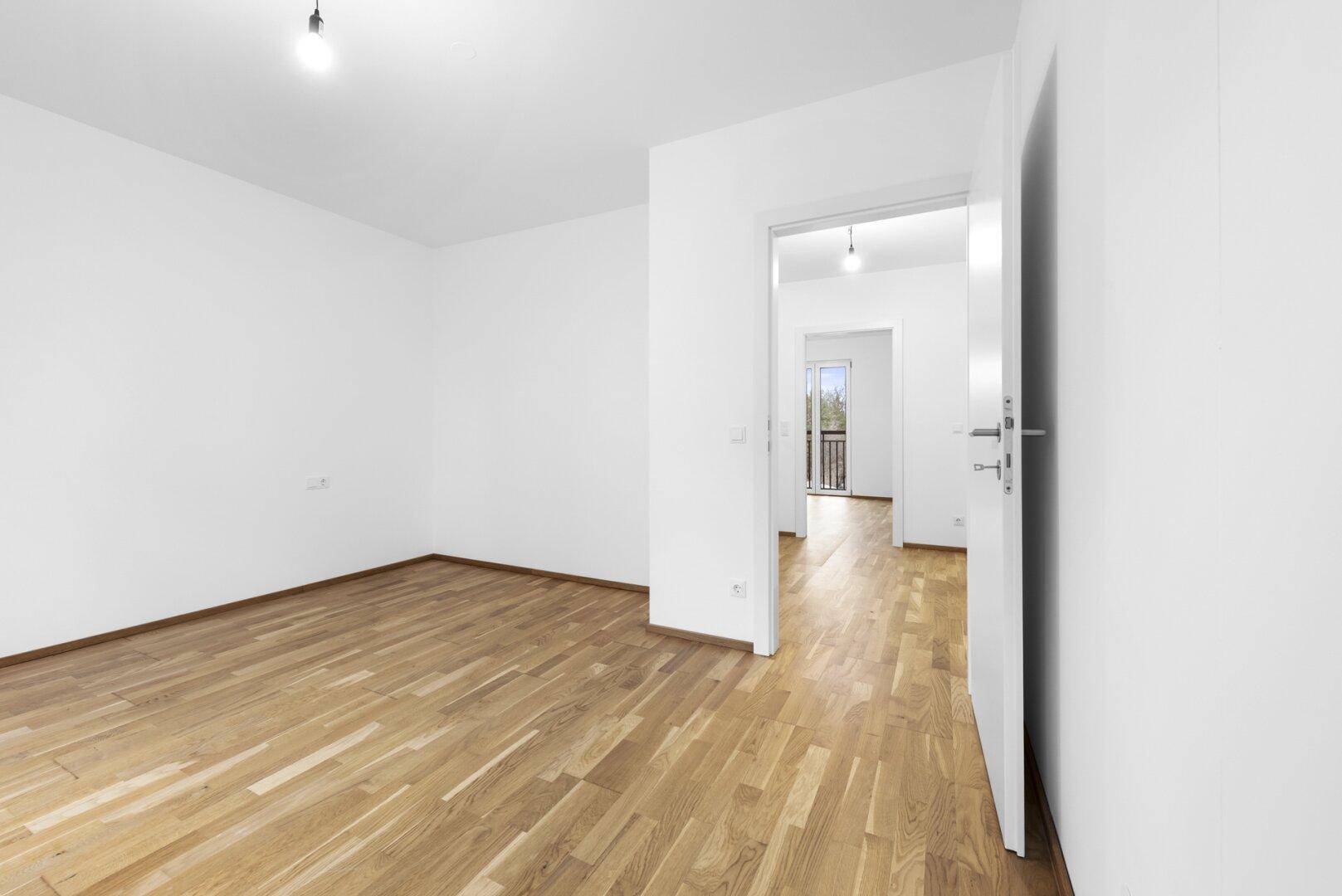 Heller Flur mit Holzboden, der zu weiteren Zimmern und einem Balkon führt.