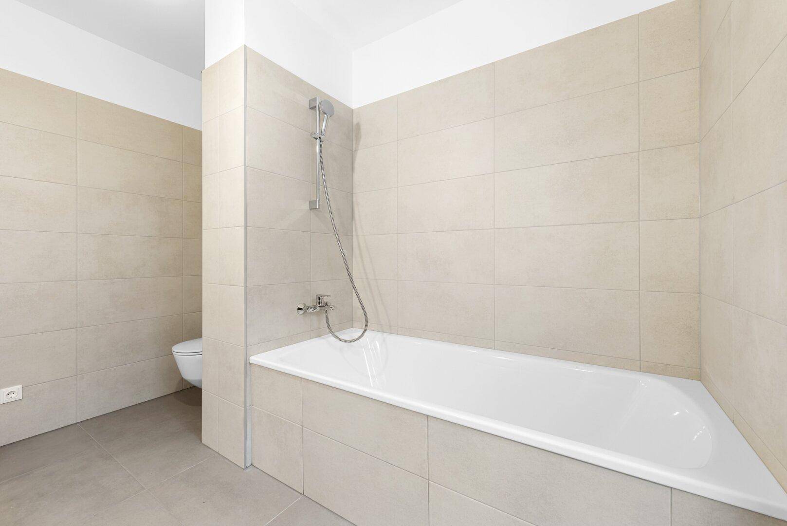 Modernes Badezimmer mit Badewanne und Duschvorrichtung, gefliest in neutralen Tönen.