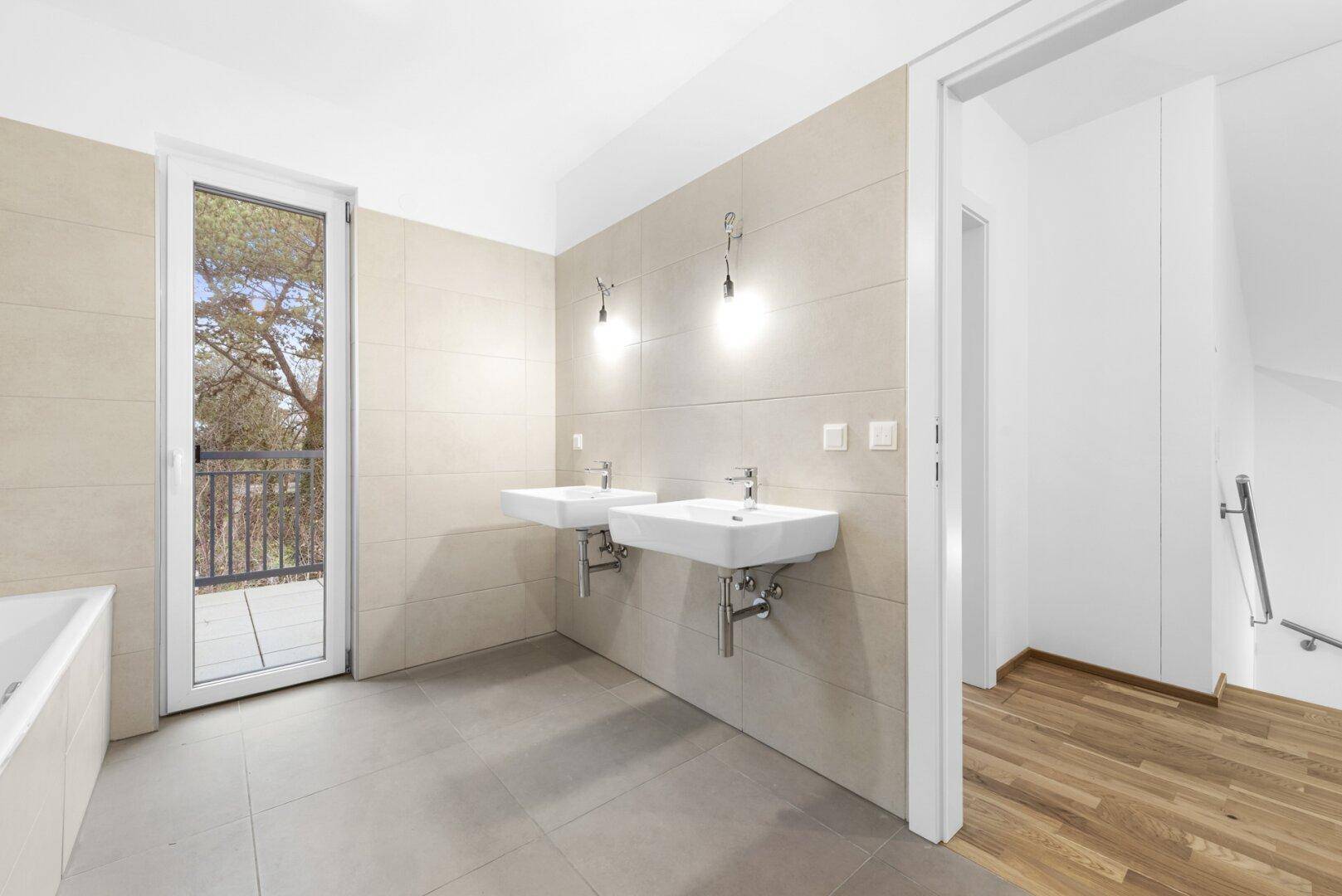 Geräumiges Badezimmer mit Doppelwaschbecken und direktem Zugang zum Balkon.