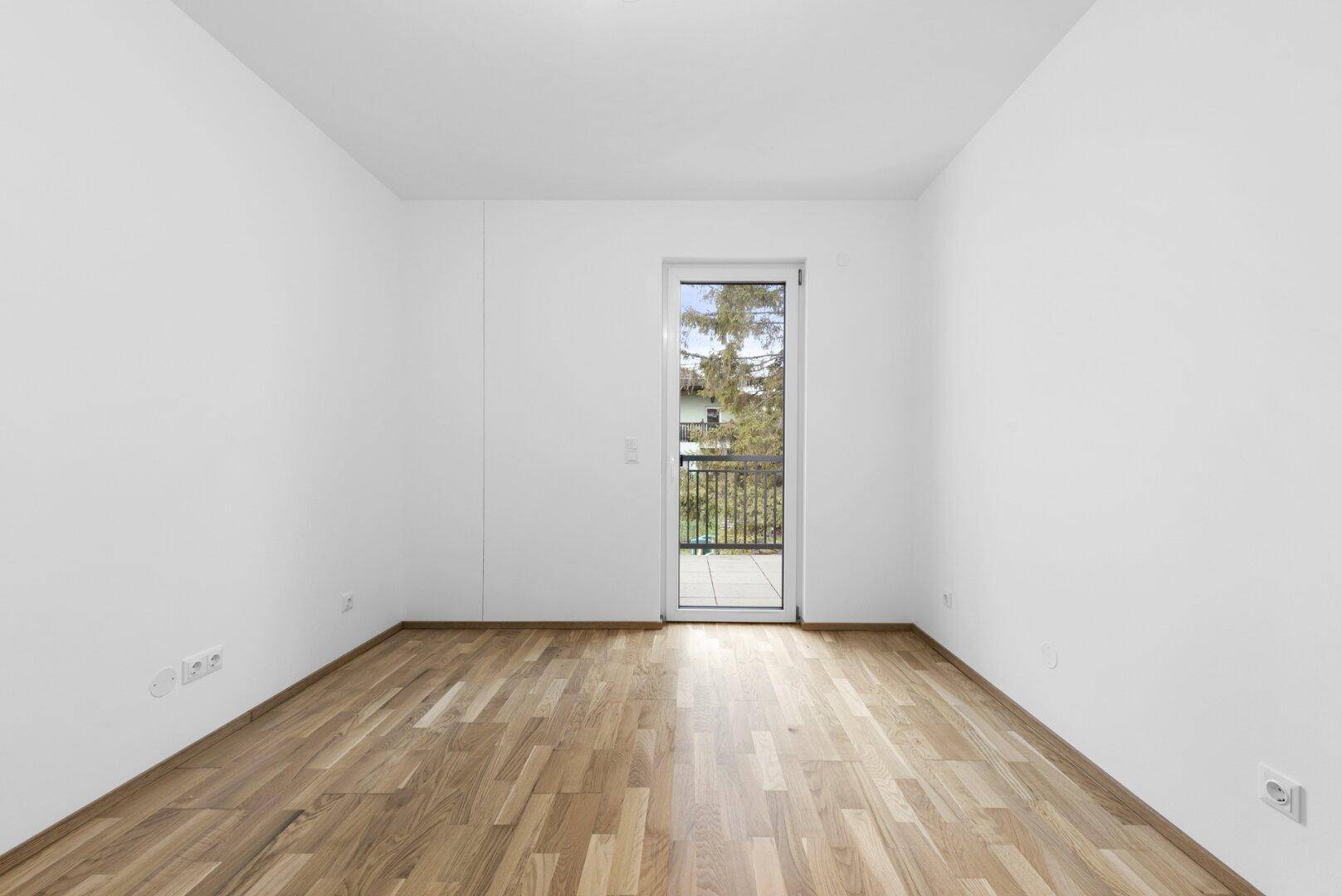 Leeres Schlafzimmer mit Holzboden und Zugang zu einem französischen Balkon.