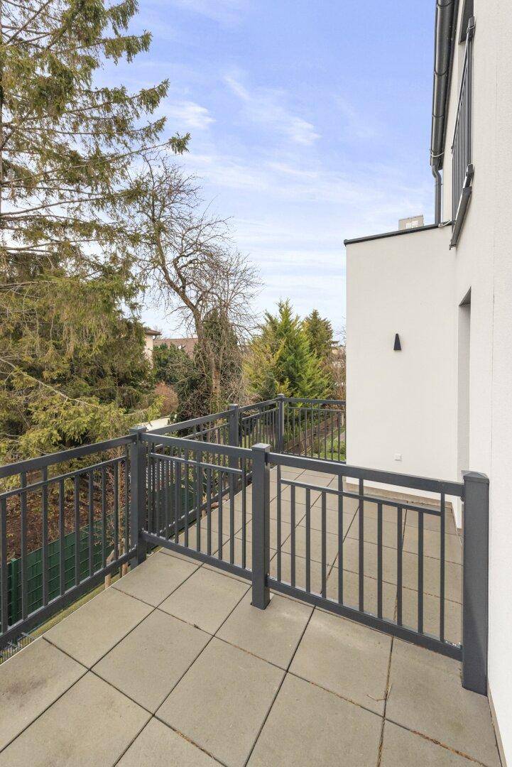 Balkon mit Fliesenboden und Metallgeländer, umgeben von hohen Bäumen.