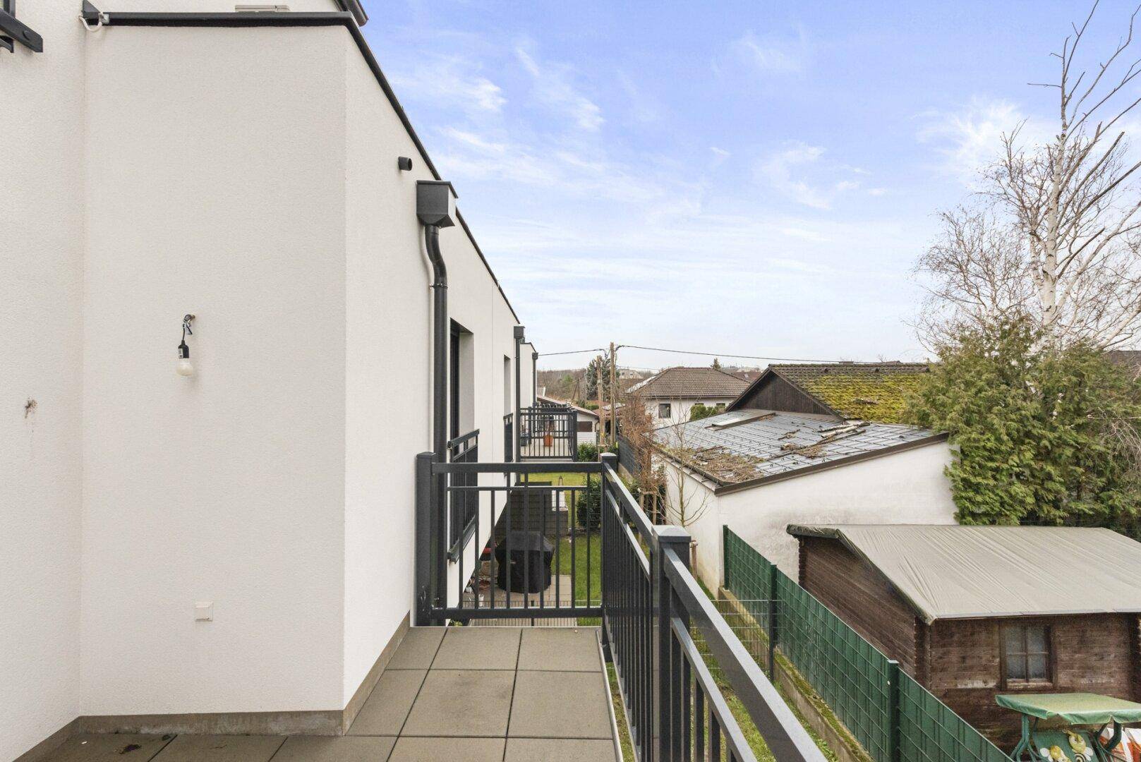 Balkon mit Fliesenboden und Blick auf die Dächer der Nachbarschaft und einen Gartenschuppen.