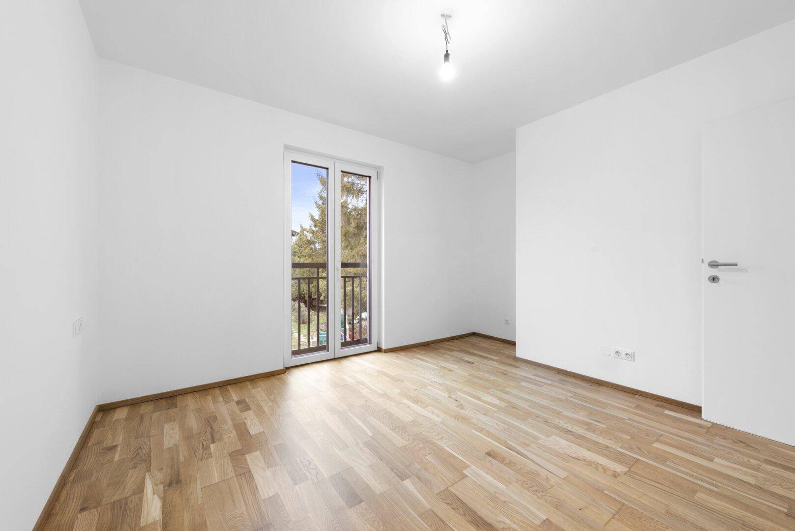 Helles Schlafzimmer mit Holzboden und Zugang zu einem französischen Balkon.