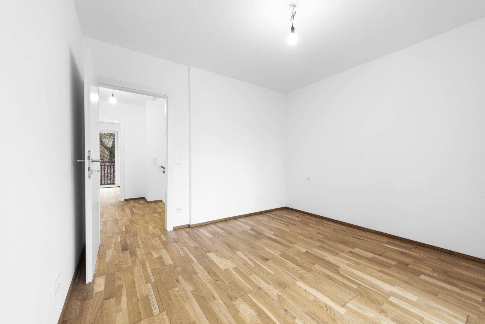 Geräumiges Zimmer mit Holzboden und Balkonzugang, gesehen vom Türrahmen.