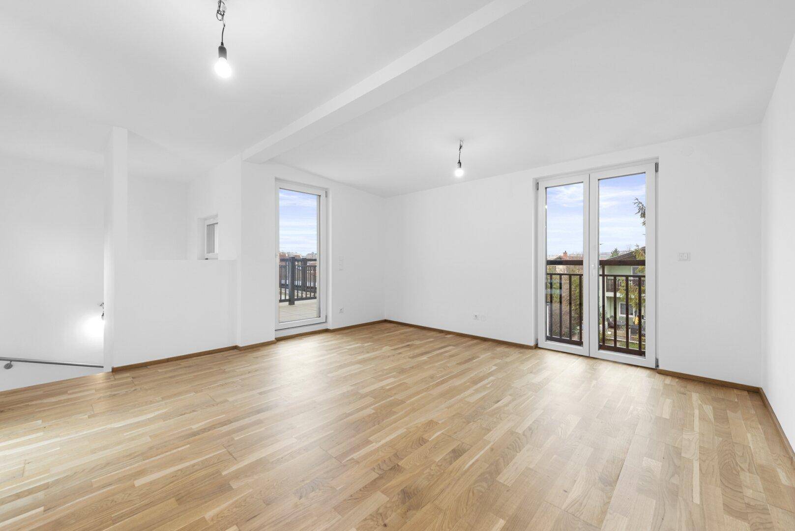Lichtdurchfluteter Raum mit Holzboden und zwei Balkonzugängen, ideal als Wohnzimmer.