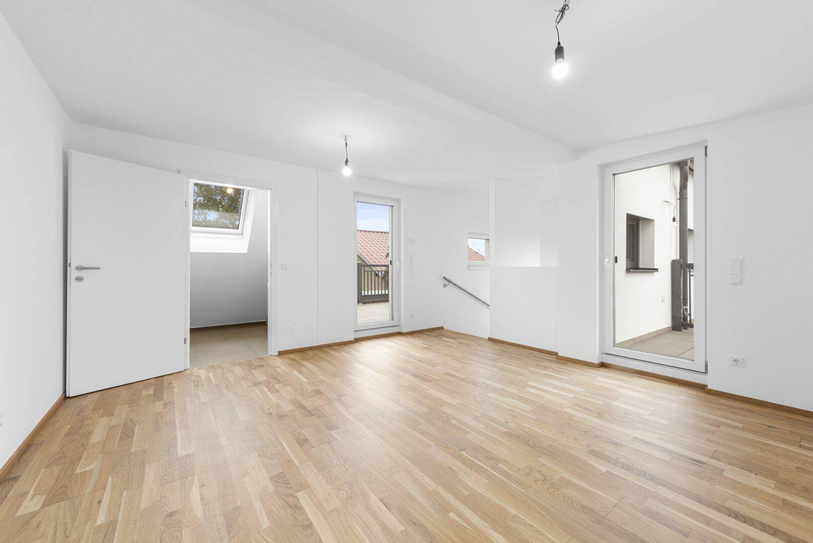 Geräumiger Wohnbereich mit Holzboden und Zugang zu einem Badezimmer mit Dachfenster.