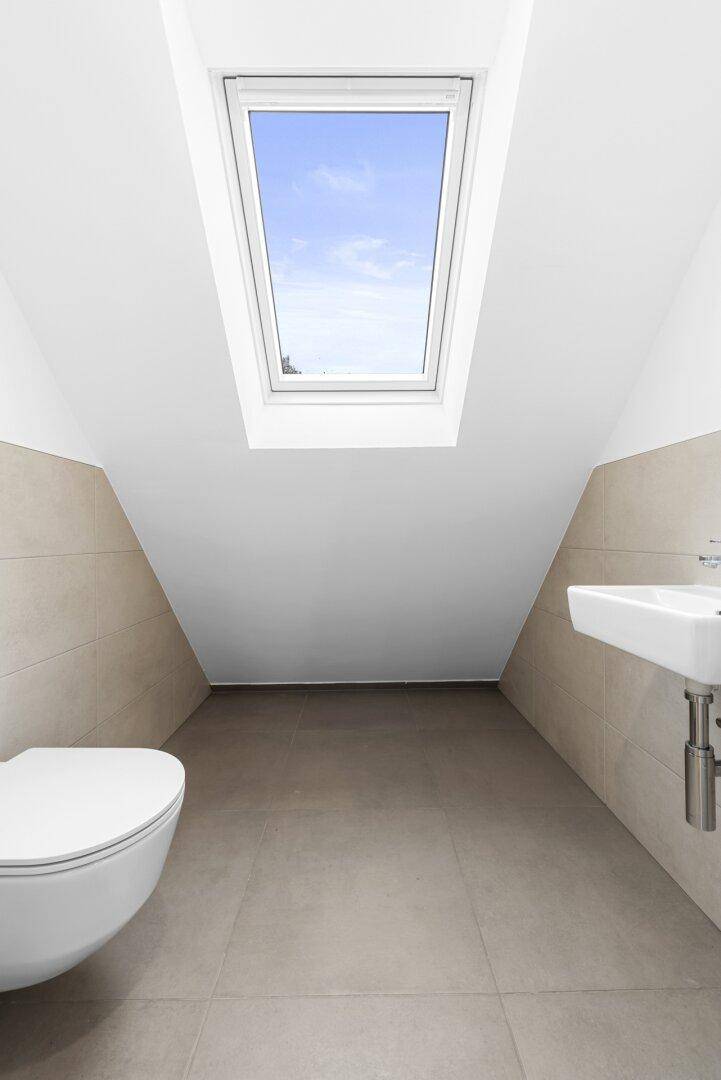 Modernes Badezimmer im Dachgeschoss mit WC, Waschbecken und großem Dachfenster.