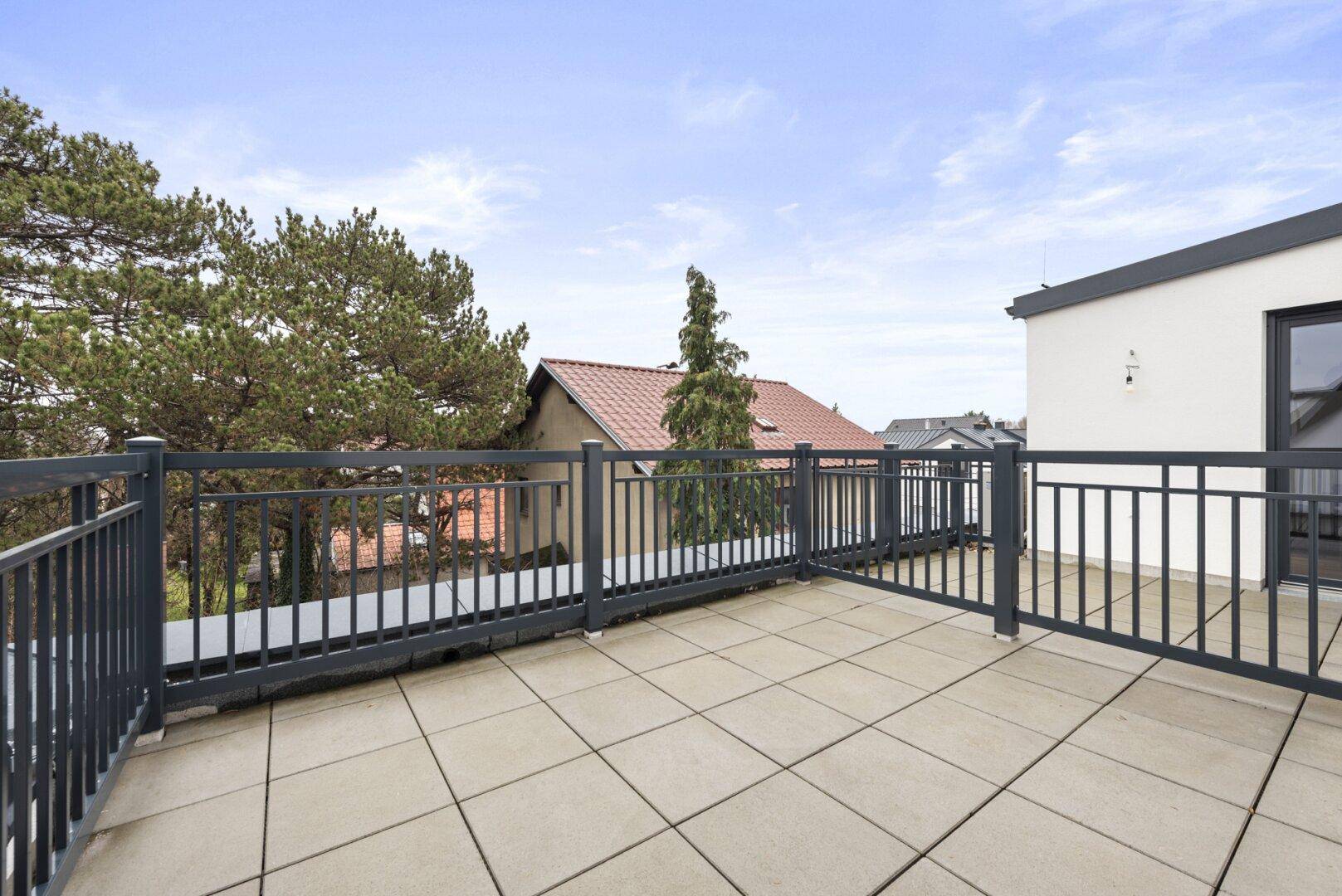 Große Dachterrasse mit Fliesenboden und Metallgeländer, bietet weite Aussicht.