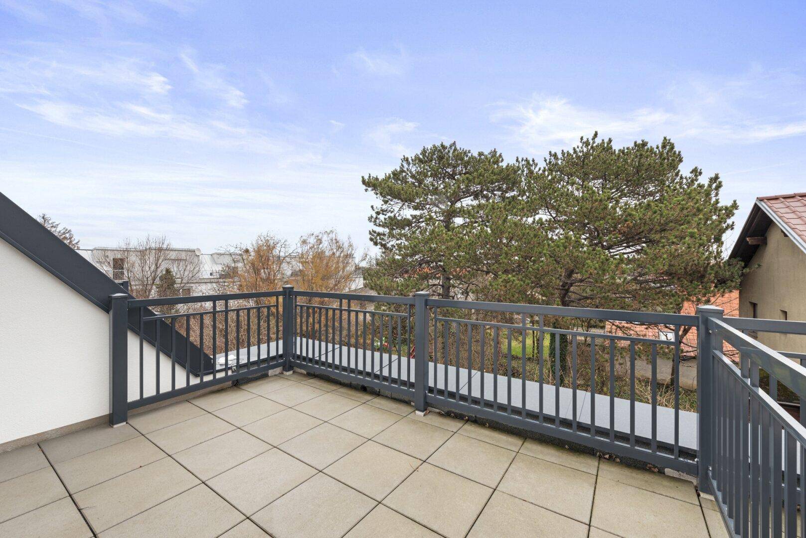 Dachterrasse mit Fliesenboden und Blick auf Bäume und die umliegende Landschaft.