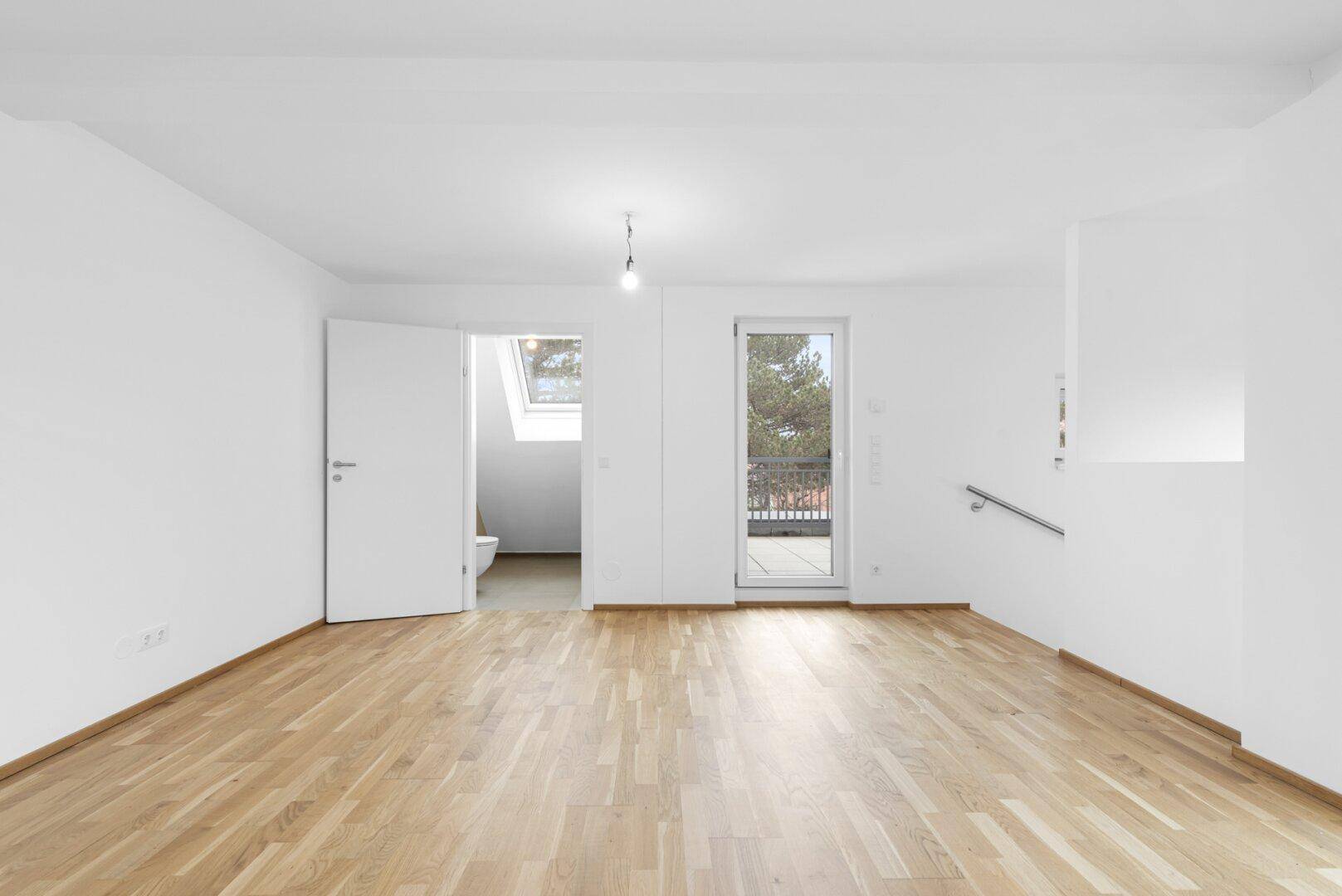Heller Wohnbereich mit Holzboden und Zugang zu einem Badezimmer mit Dachfenster.