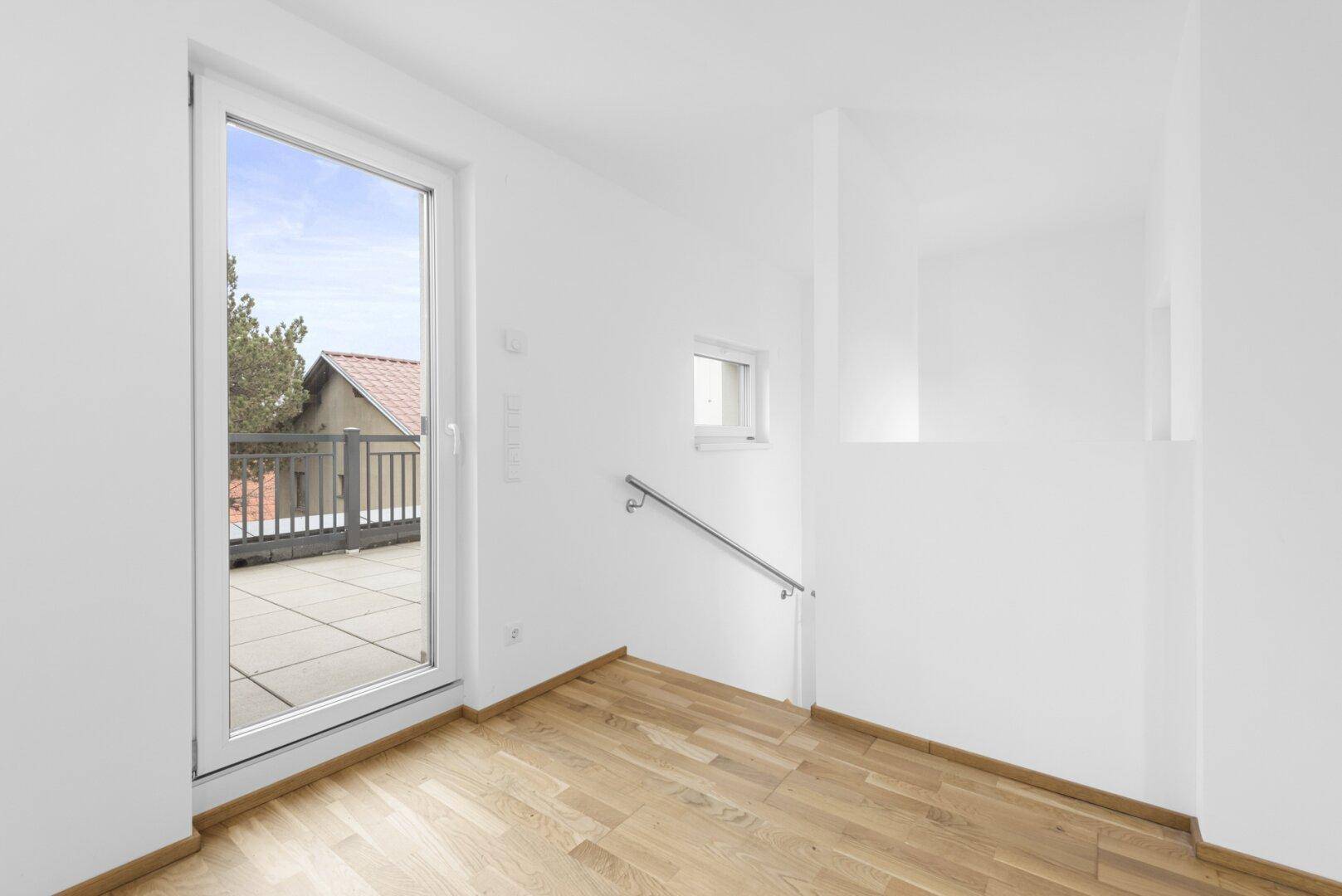 Geräumiger Wohnbereich mit Holzboden und Zugang zu einem sonnigen Balkon.