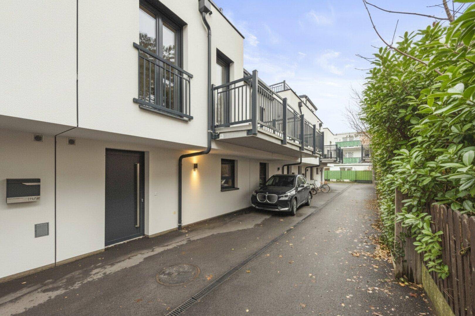Moderne Reihenhäuser mit Balkonen und Zufahrt, ein Auto ist geparkt.