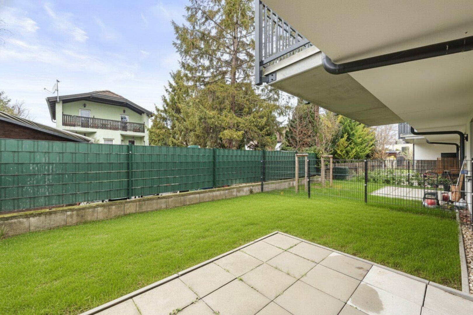 Gepflegter Gartenbereich mit Rasenfläche und gepflasterter Terrasse hinter dem Haus.