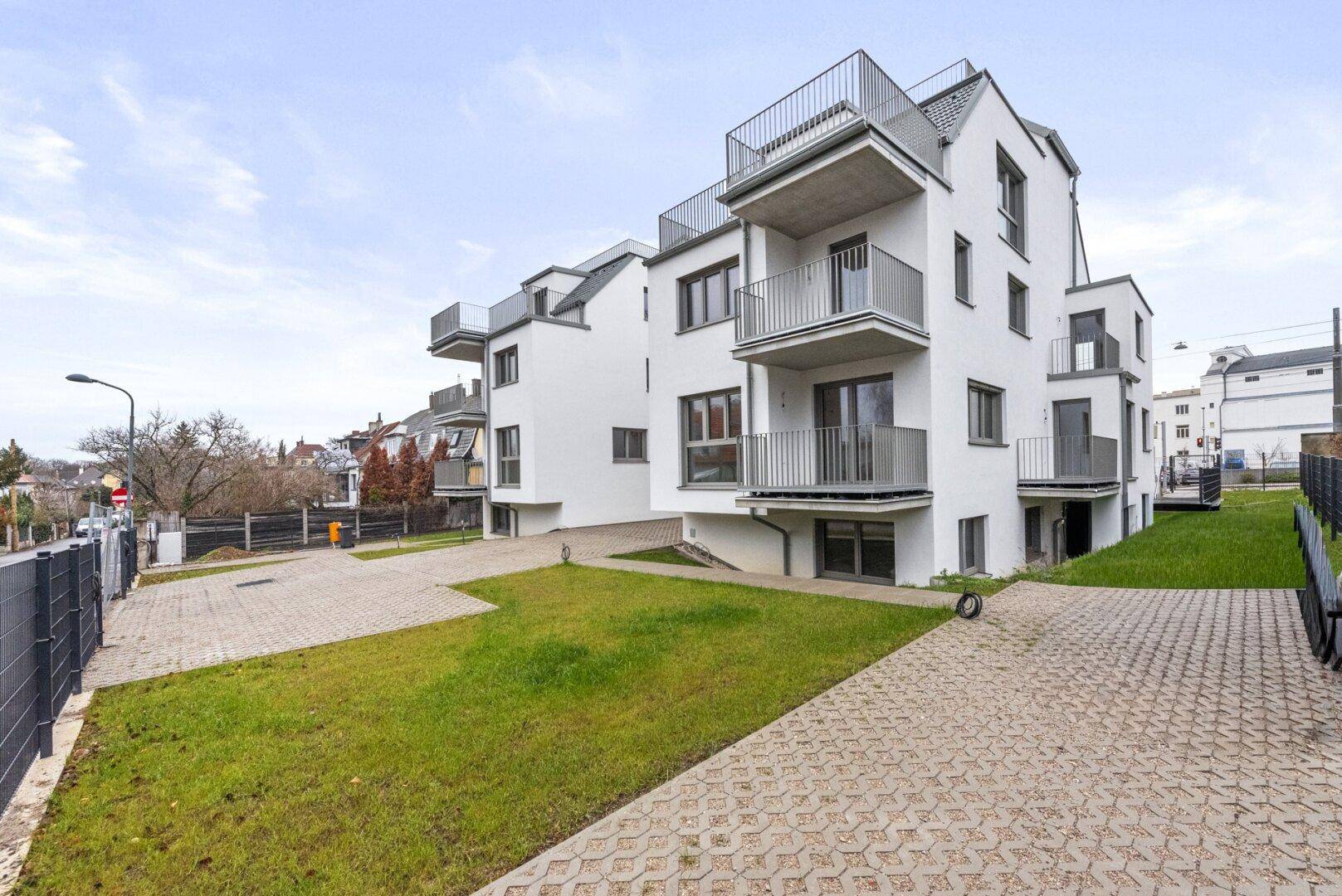 Ansicht eines modernen weißen Wohngebäudes mit Balkonen, Dachterrassen und gepflegter Außenanlage.