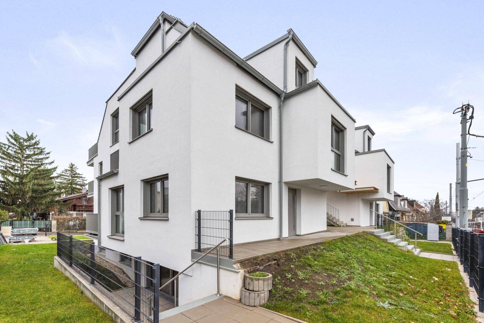 Seitenansicht eines modernen weißen Wohnhauses mit großen Fenstern und einem leicht abfallenden Gartenbereich.