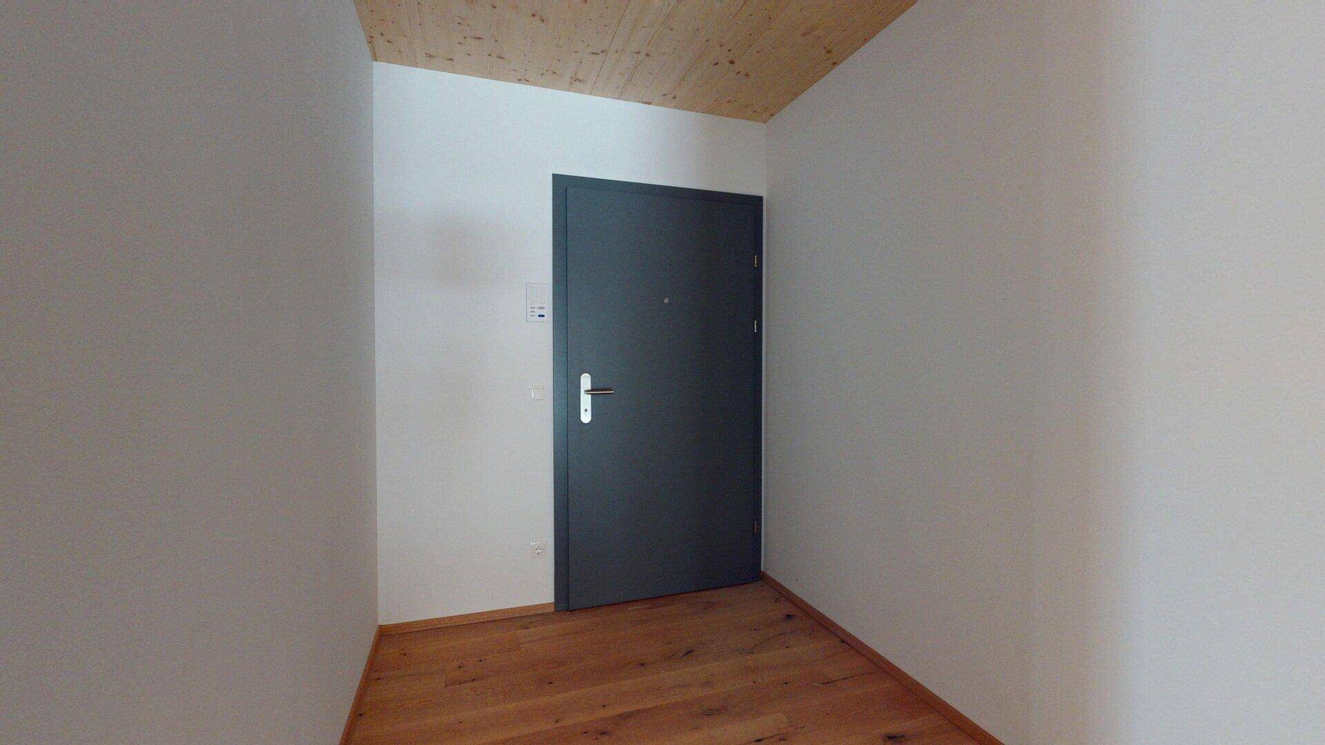 Heller Eingangsbereich mit Holzboden und dunkler Eingangstür, führt in die Wohnräume.
