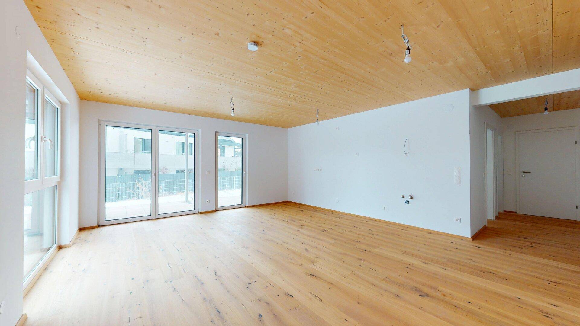 Heller, leerer Wohnraum mit Holzboden und großen Fensterfronten, bereit für die Einrichtung.