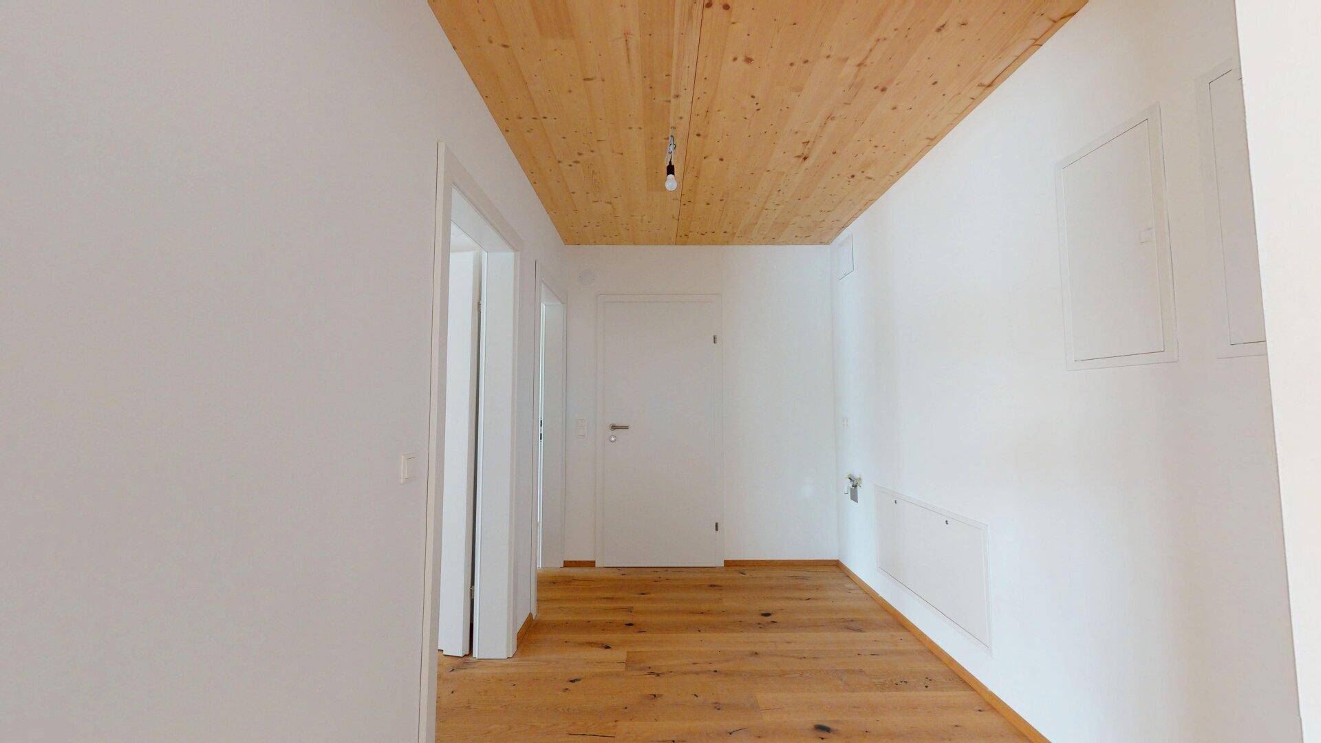 Heller Flur mit Holzboden und Holzbalkendecke, verbindet verschiedene Räume im Neubau.
