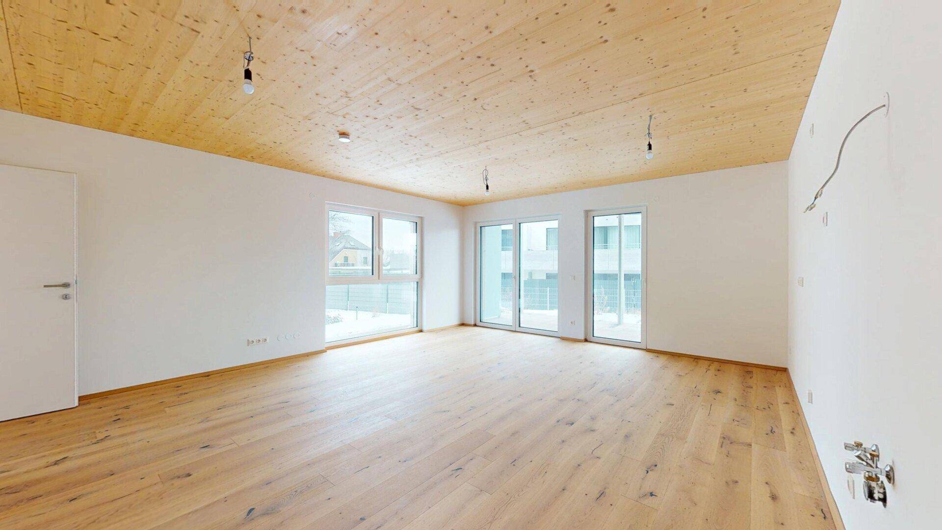 Lichtdurchfluteter Wohnbereich mit Holzboden und breiten Fensterfronten, bietet viel Platz.