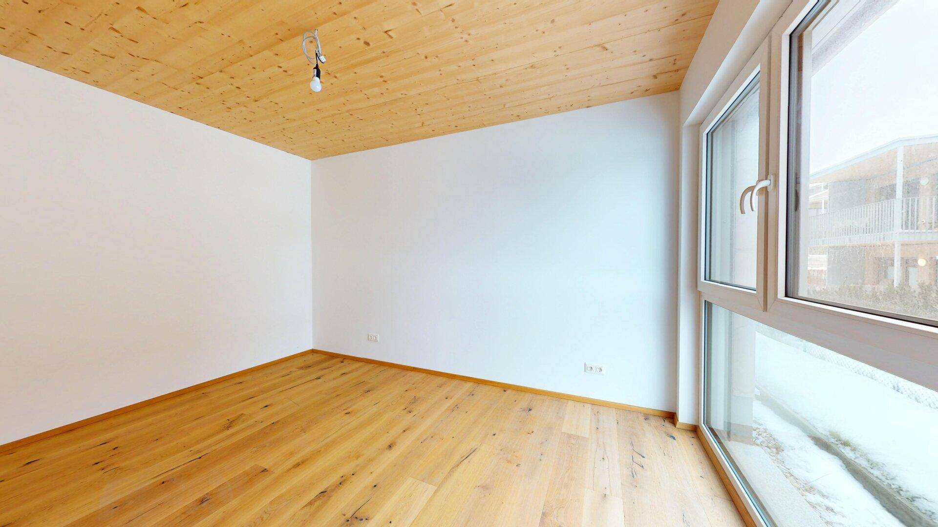 Geräumiges Zimmer mit Holzboden und großem Fenster, bietet viel Tageslicht und eine angenehme Atmosphäre.