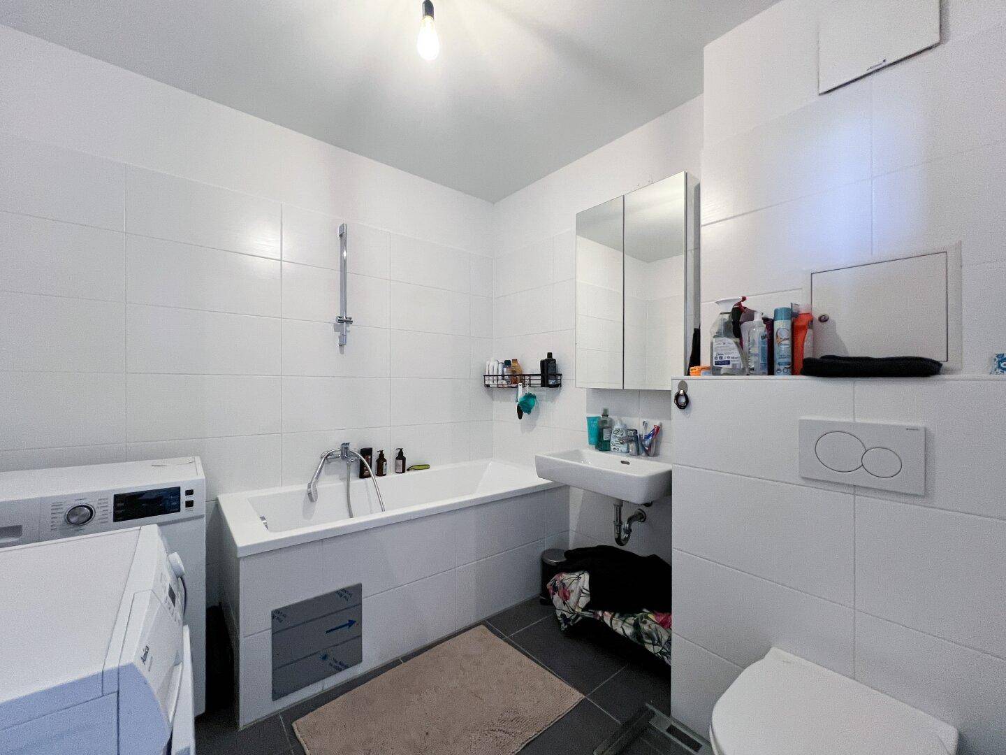 Modernes Badezimmer mit Badewanne, WC und Waschmaschinenanschluss.