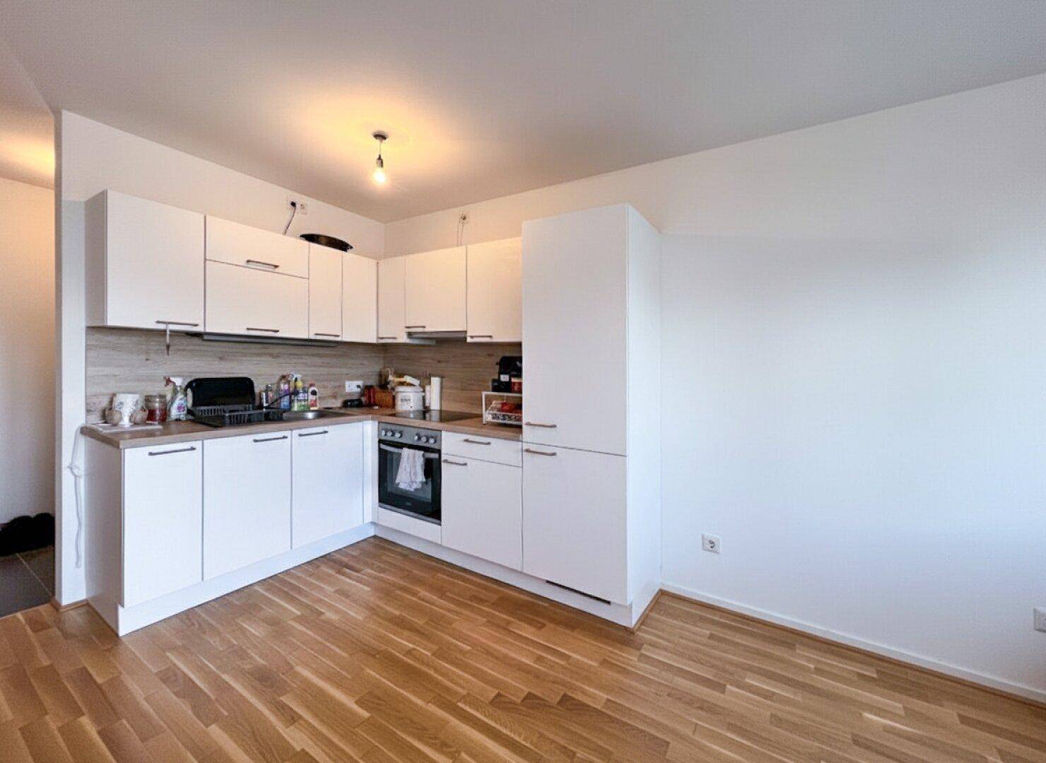 Moderne Einbauküche mit weißen Schränken, Holz-Arbeitsplatte und Parkettboden in hellem Raum.