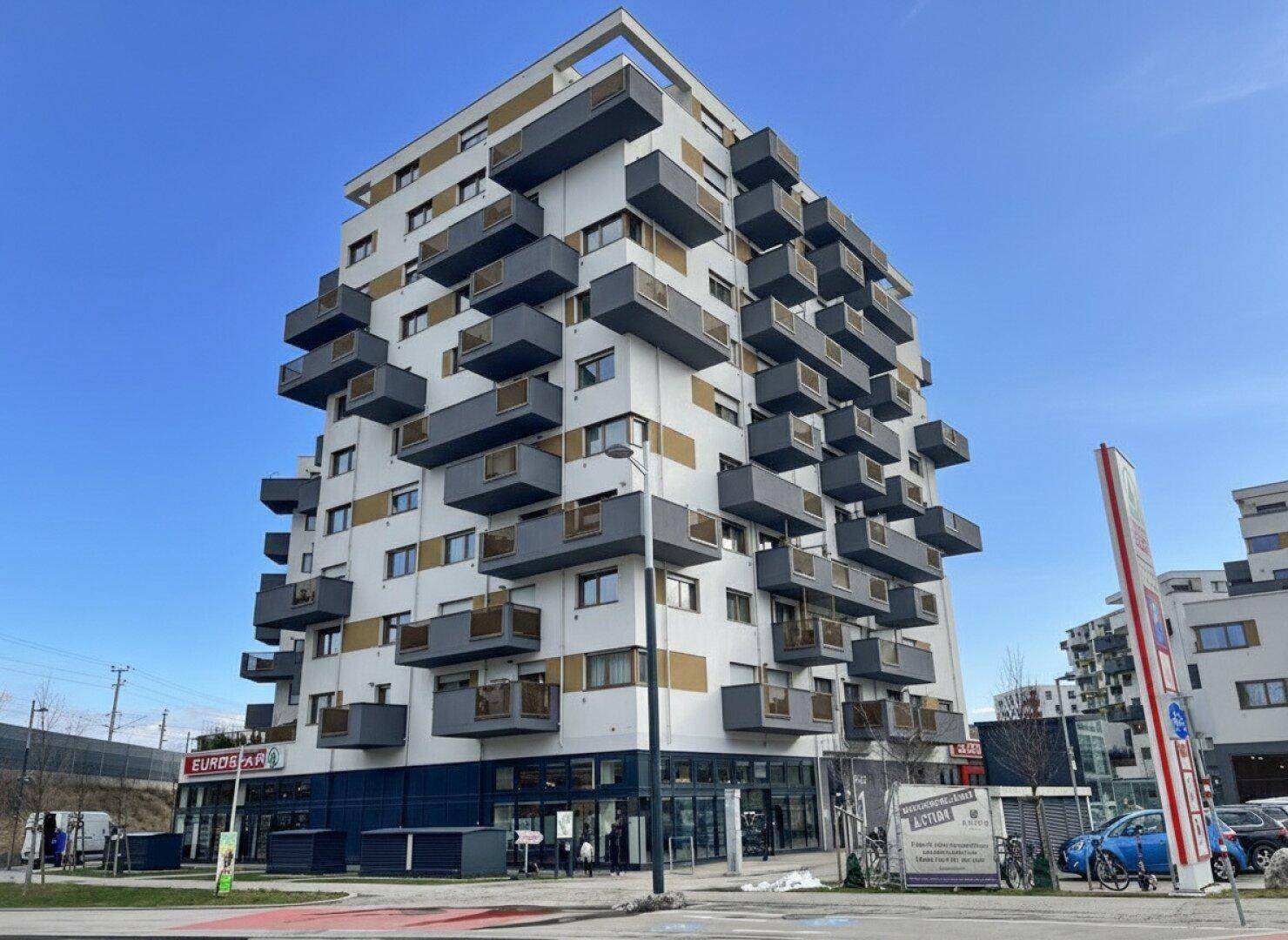 Modernes Wohngebäude mit vielen Balkonen und Geschäften im Erdgeschoss.