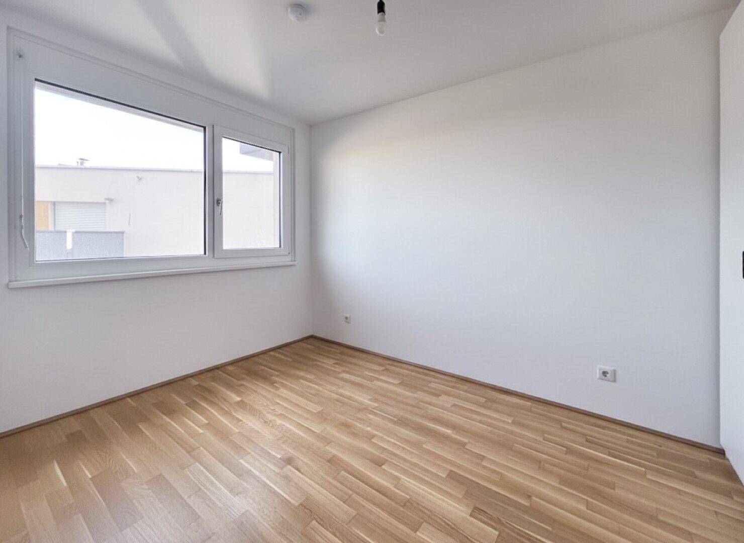 Helles Schlafzimmer mit Parkettboden und großem Fenster für viel Tageslicht.