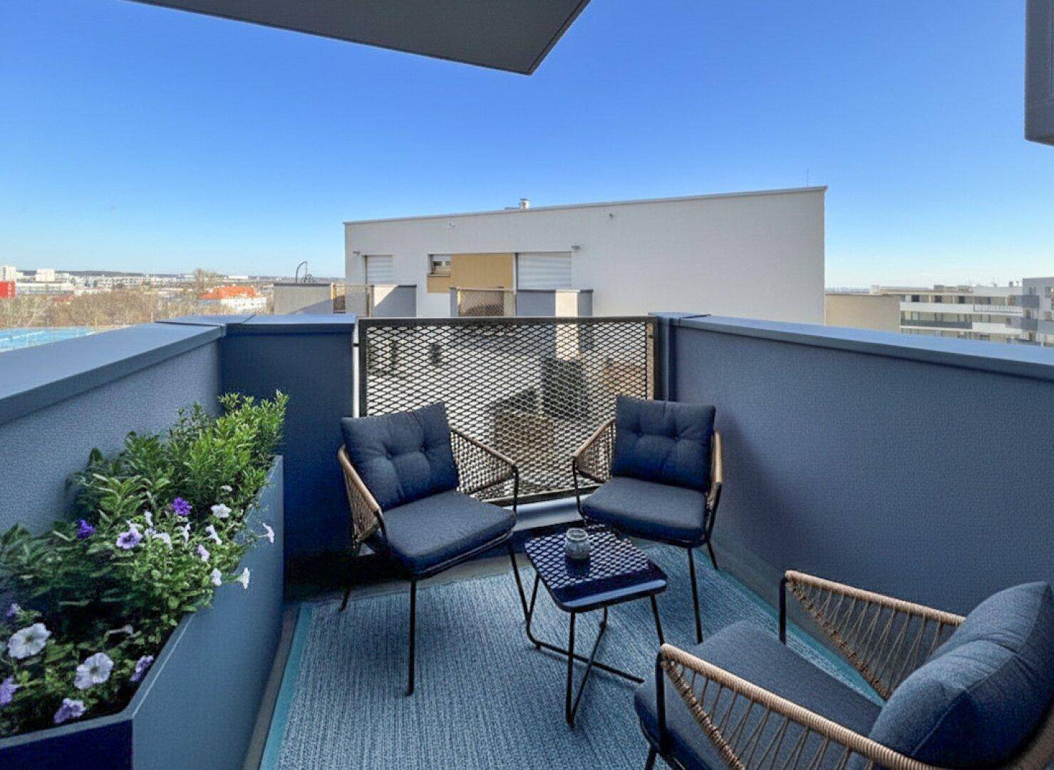 Sonniger Balkon mit bequemen Stühlen, Blumenkästen und weitem Blick über die Stadt.
