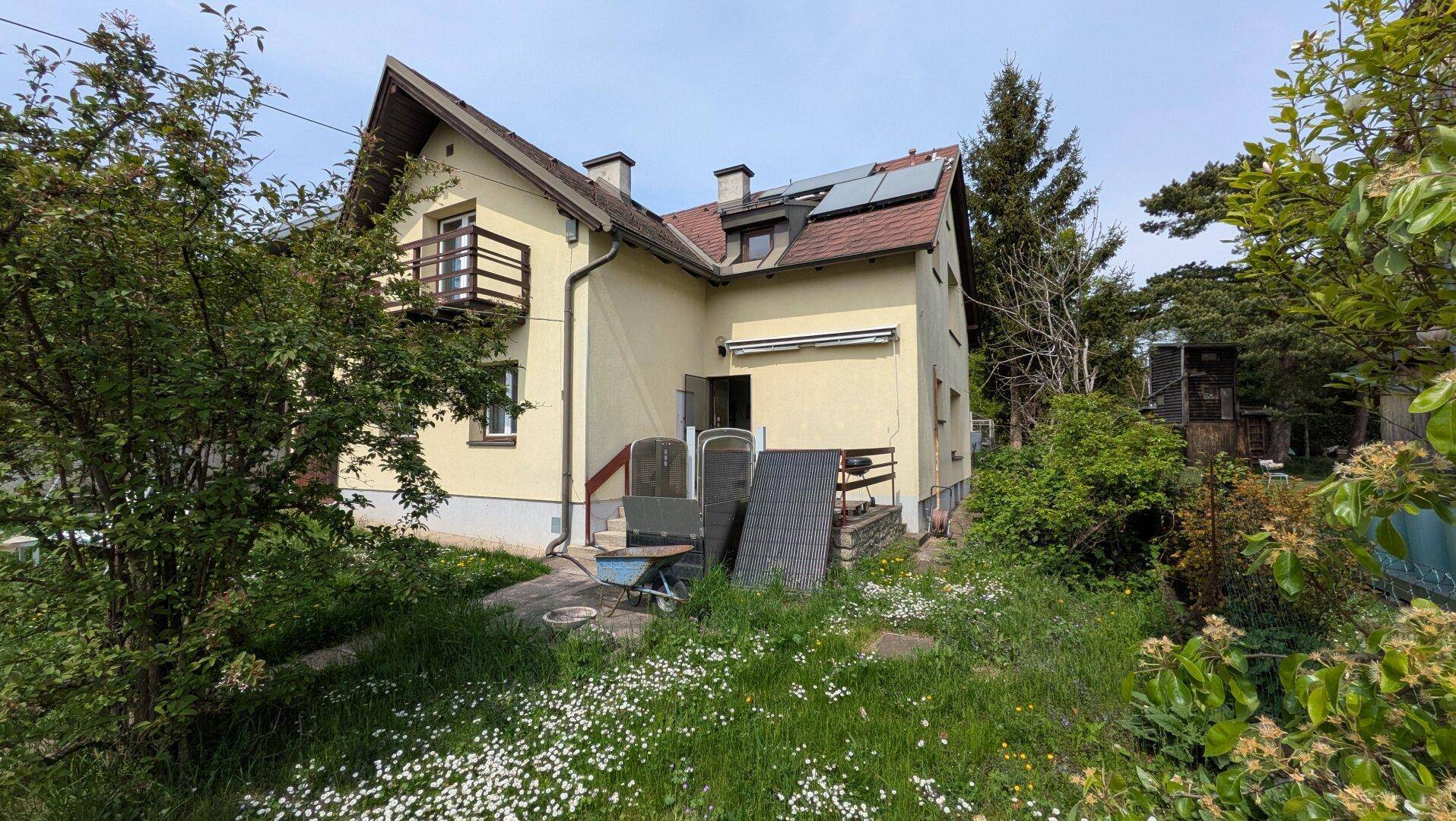 Rückseite des Hauses mit einer kleinen Terrasse, Gartenmöbeln und Photovoltaikanlage auf dem Dach.