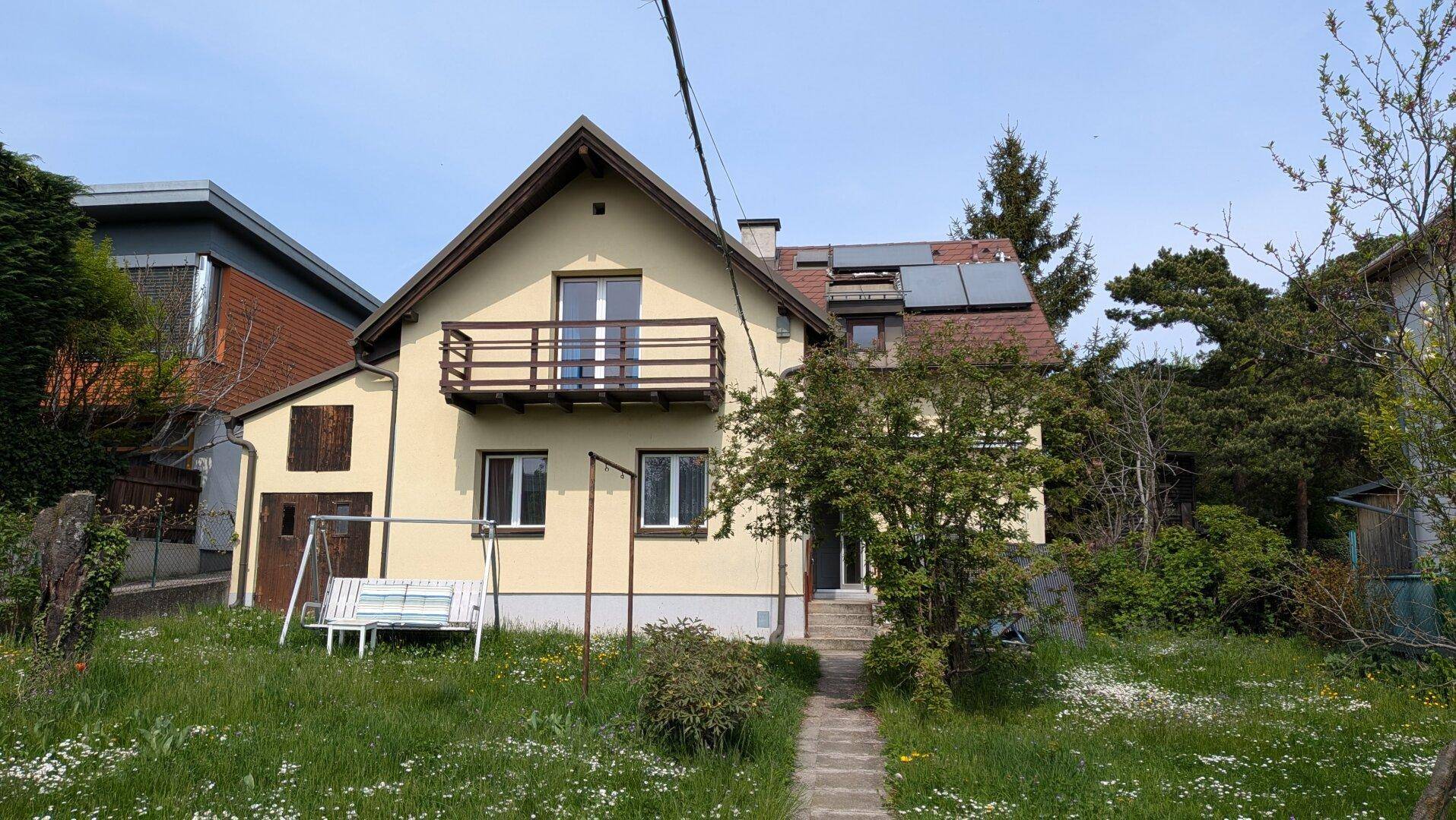 Vorderseite des Hauses mit Balkon, einer Schaukel und einem gepflegten Vorgarten.