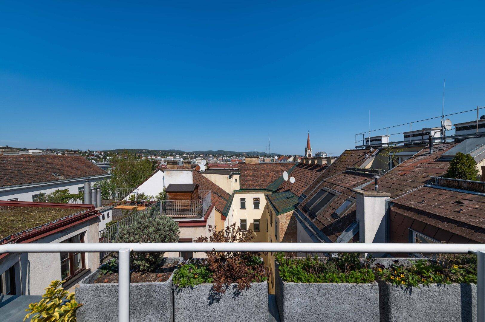 Geräumige Dachterrasse mit Stadtblick und Pflanzkübeln unter blauem Himmel.