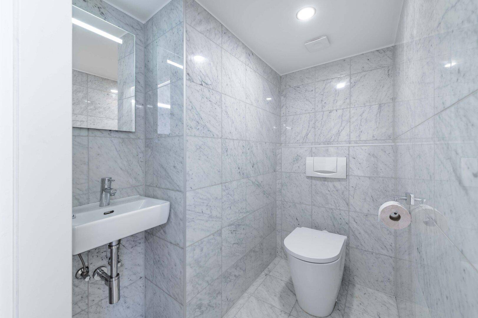 Modernes Gäste-WC mit Marmorfliesen, wandhängendem WC und kleinem Waschbecken.