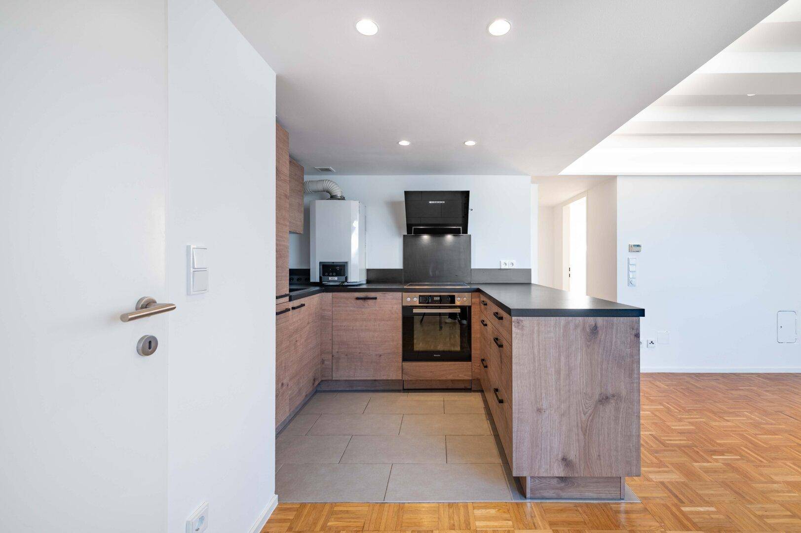 Moderne Einbauküche mit Holzfronten, dunkler Arbeitsplatte und integriertem Backofen.