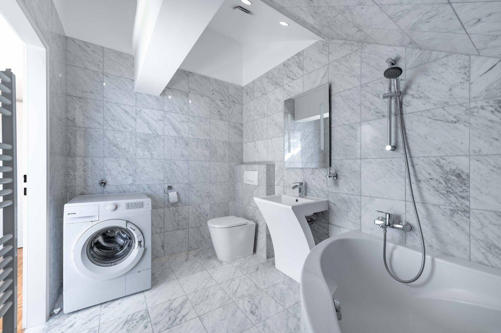 Modernes Badezimmer mit Marmorfliesen, Badewanne, WC und Waschmaschine.