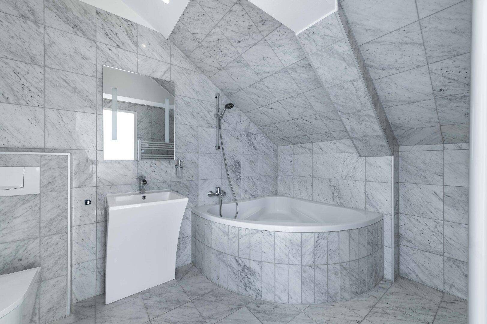 Helles Badezimmer mit Marmorfliesen, Eckbadewanne und modernem Waschbecken.