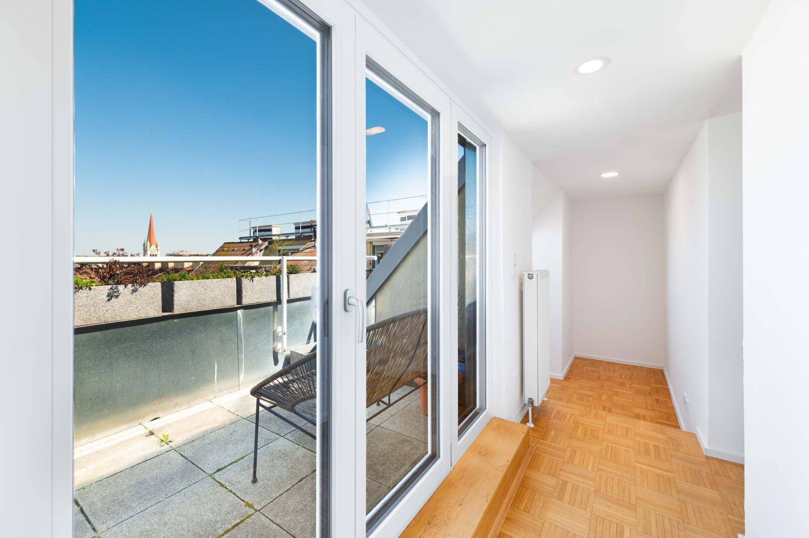 Heller Flur mit Zugang zu einer Terrasse und Blick auf die Stadt.
