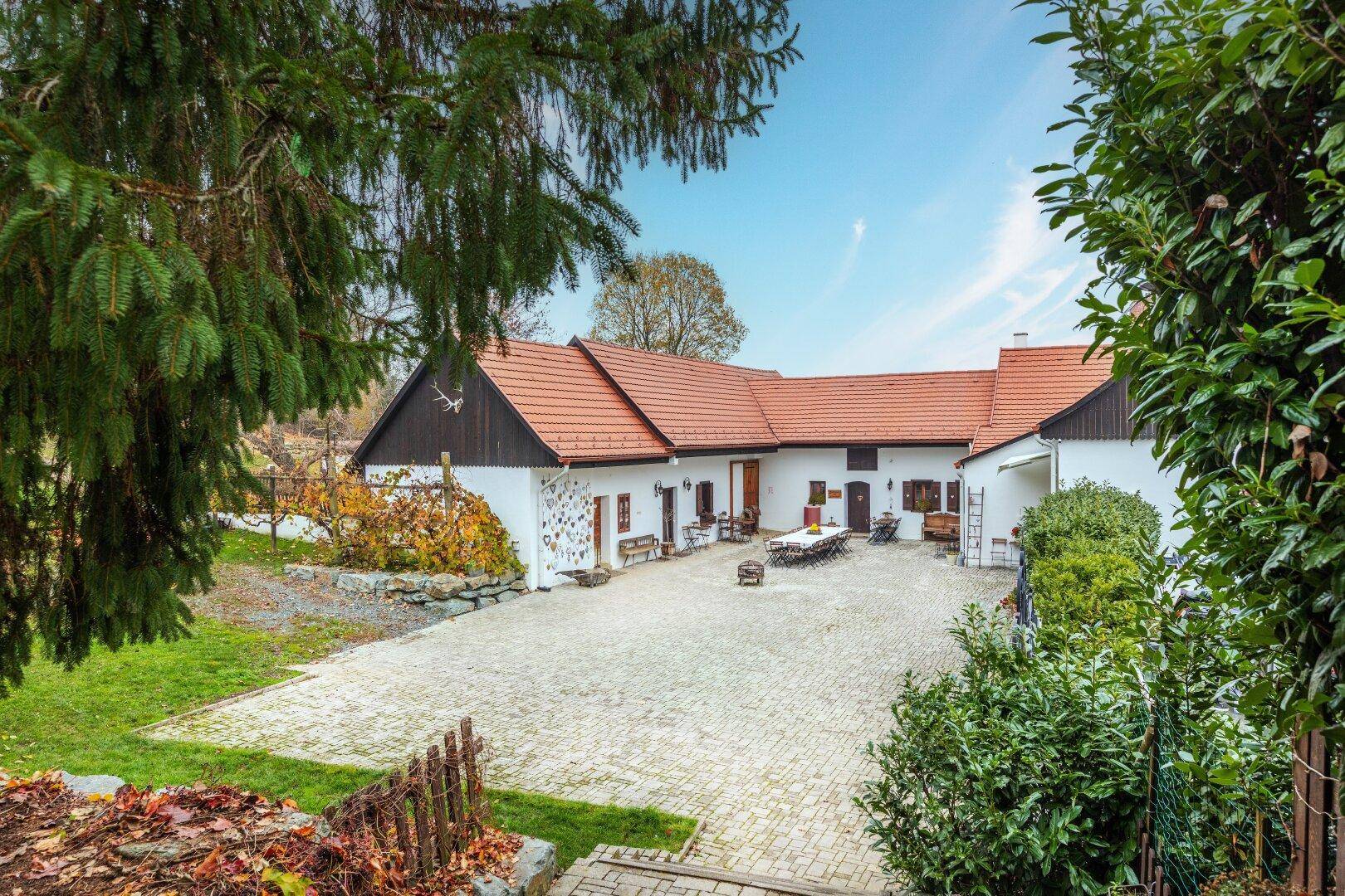 Weitläufiger gepflasterter Innenhof mit Sitzgelegenheiten, umgeben von traditionellen Gebäuden und grüner Landschaft.
