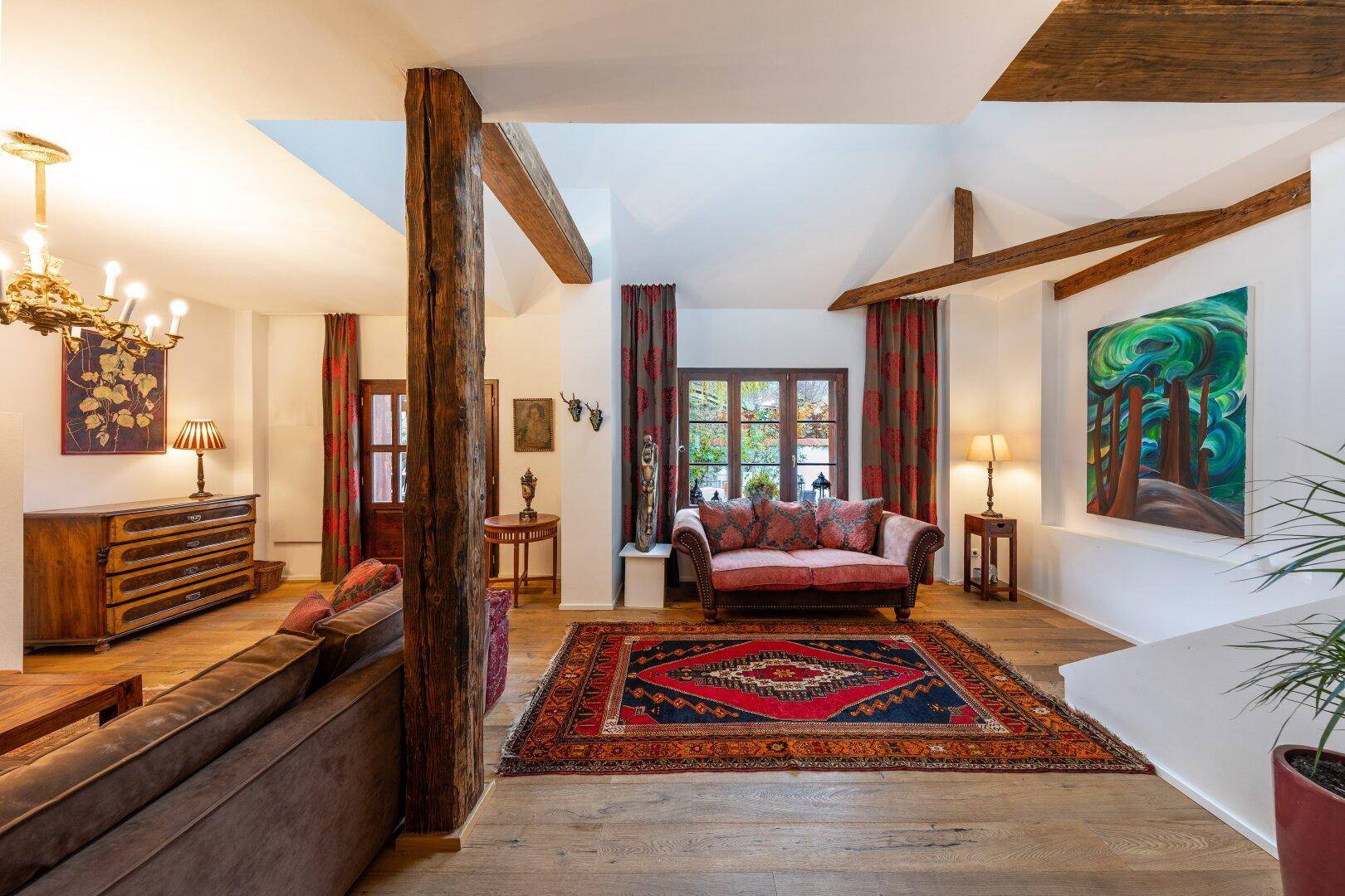 Großzügiges Wohnzimmer mit hohen Decken, Holzbalken und einem großen Teppich auf Parkettboden.