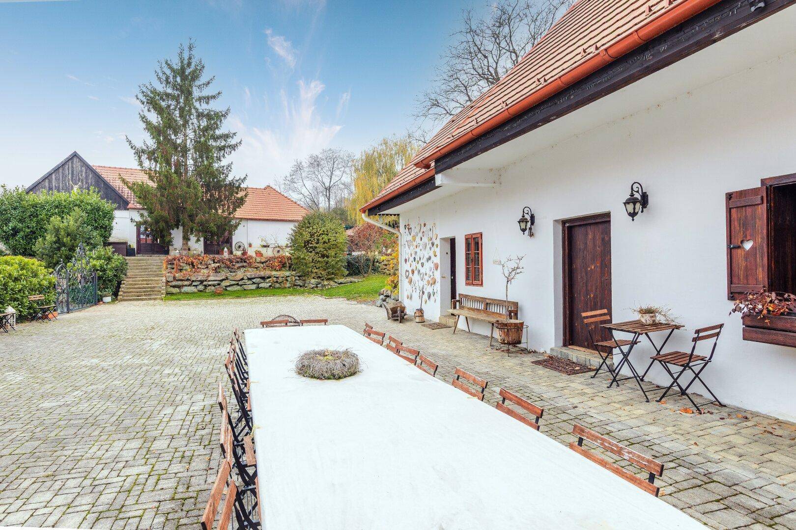 Langer Tisch im gepflasterten Innenhof, umgeben von traditionellen Gebäuden und grüner Umgebung.