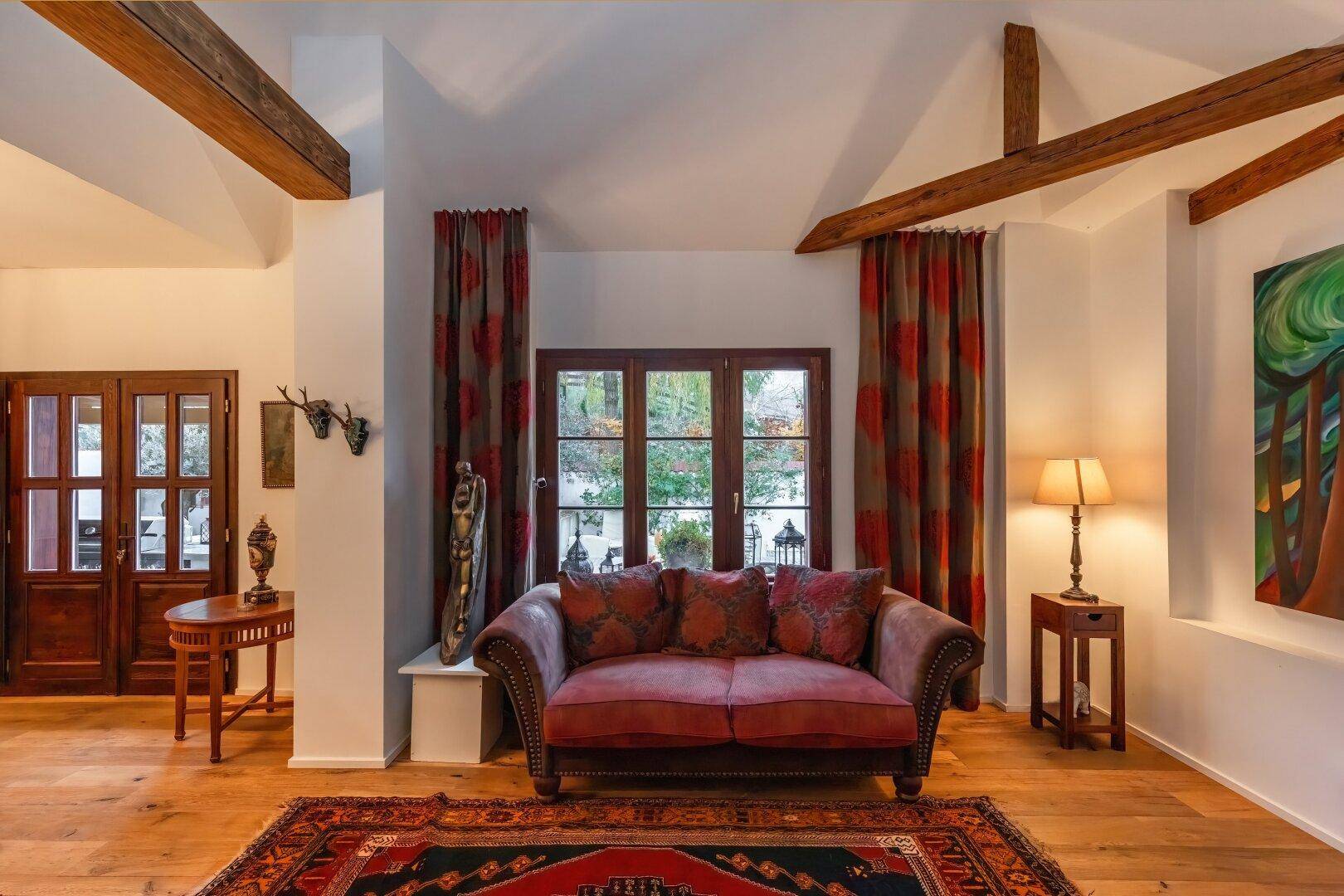 Helles Wohnzimmer mit Sofa, Holzbalken und großem Fenster mit Blick ins Grüne.