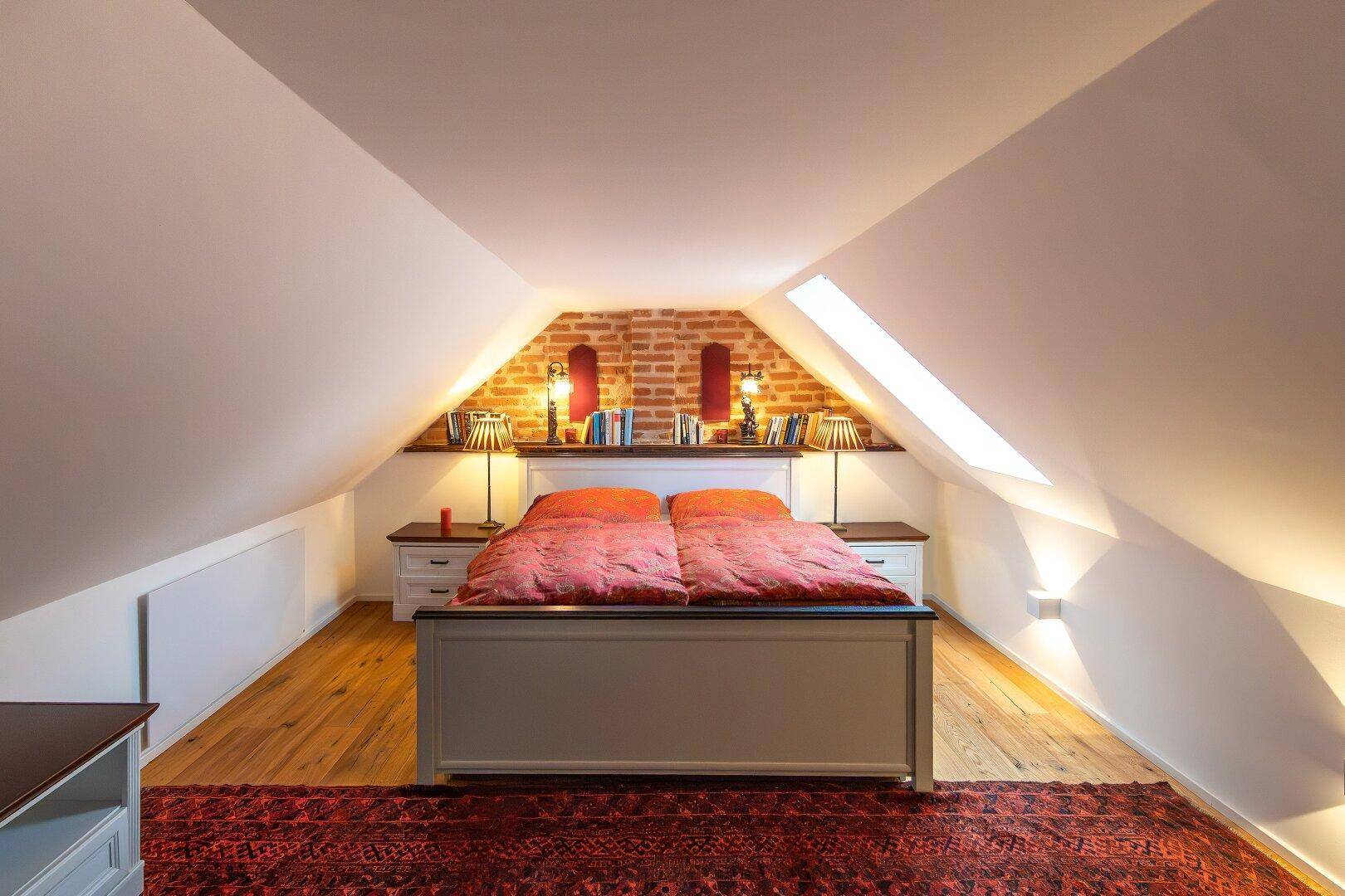 Dachschlafzimmer mit Doppelbett, freigelegter Ziegelwand und Dachfenstern für natürliches Licht.