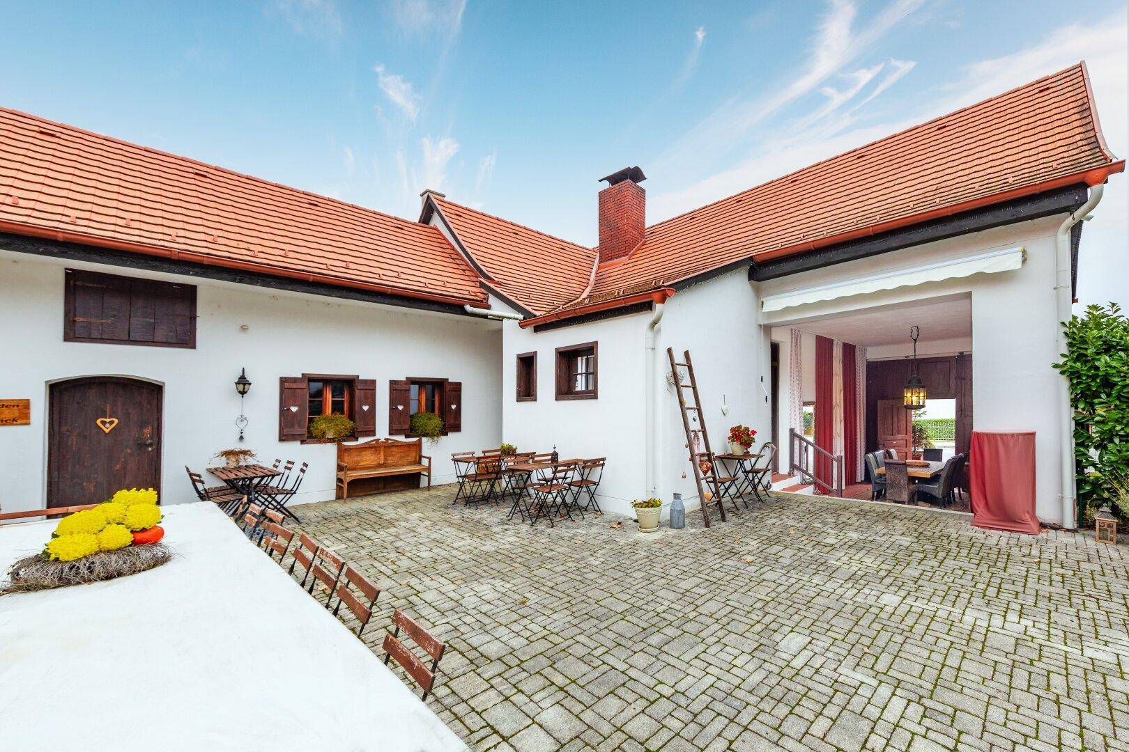 Blick über den Innenhof mit langen Tischen und Stühlen, angrenzend an einen überdachten Eingangsbereich.